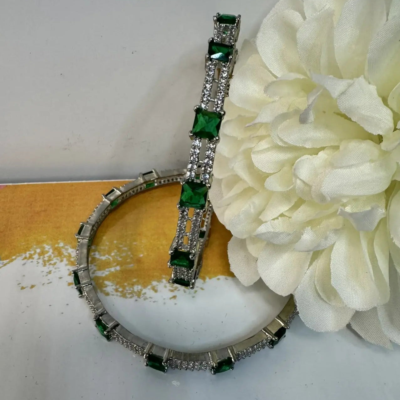 bangles with green gemstones and American diamonds on a white surface with a white flower.