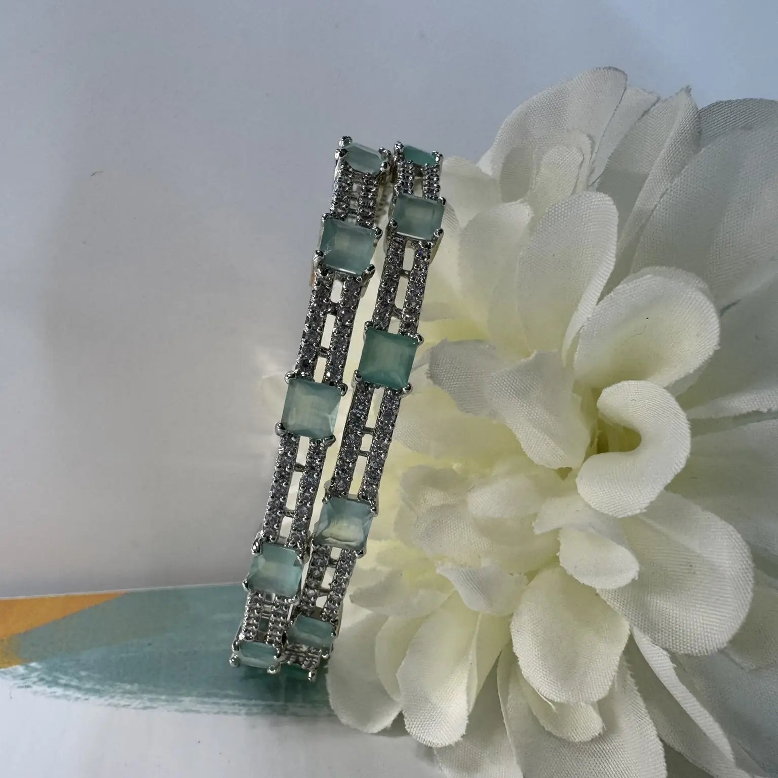 Bangles with teal gemstones on a white flower