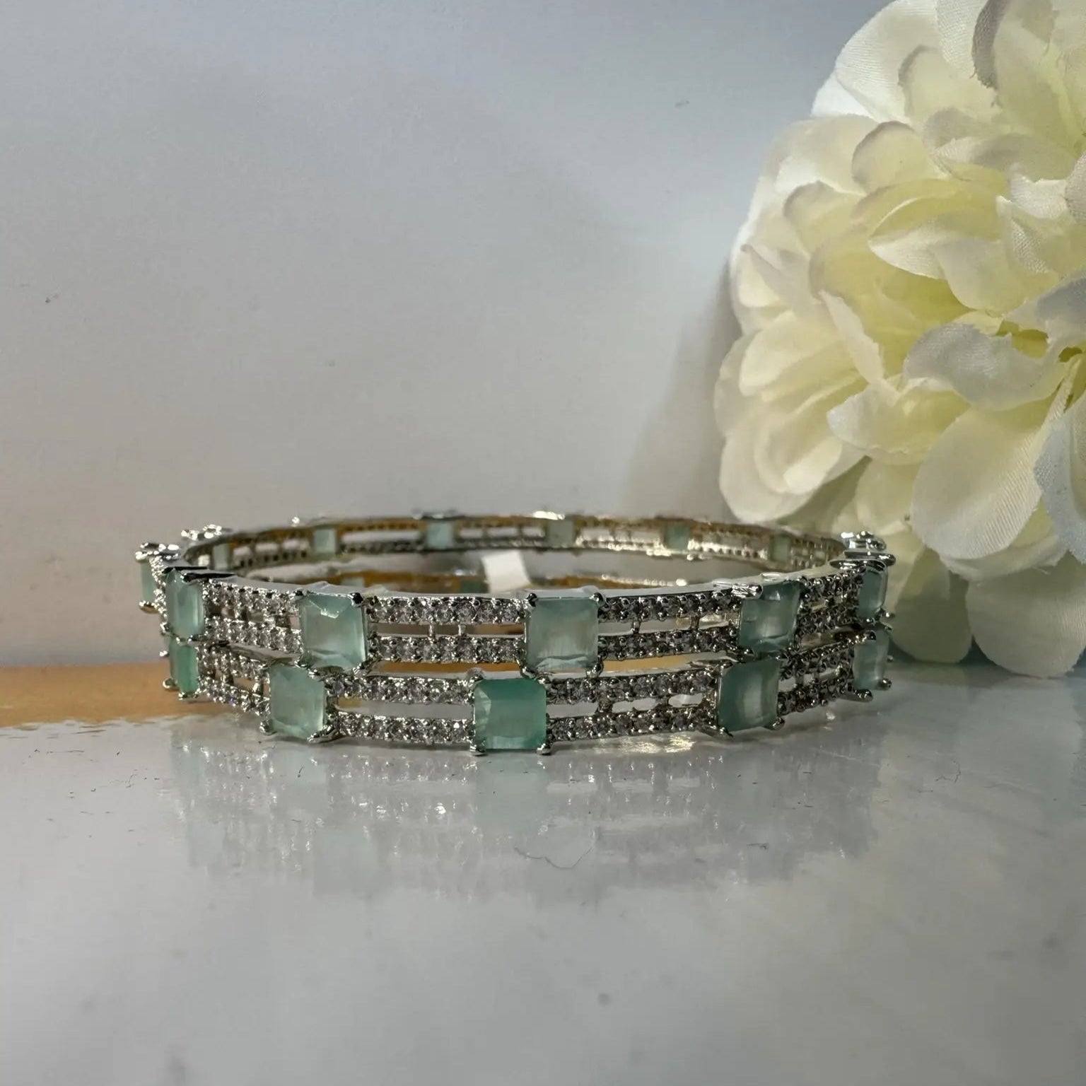 Silver bangles with teal gemstones on a light surface with a white flower in the background