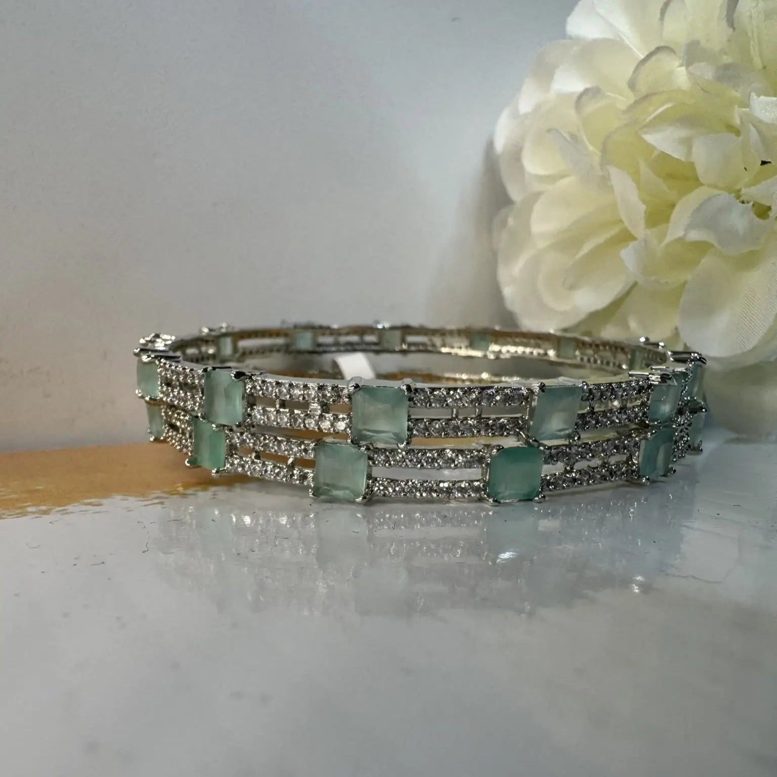 Bangles with teal gemstones on a marble surface with flower in the background