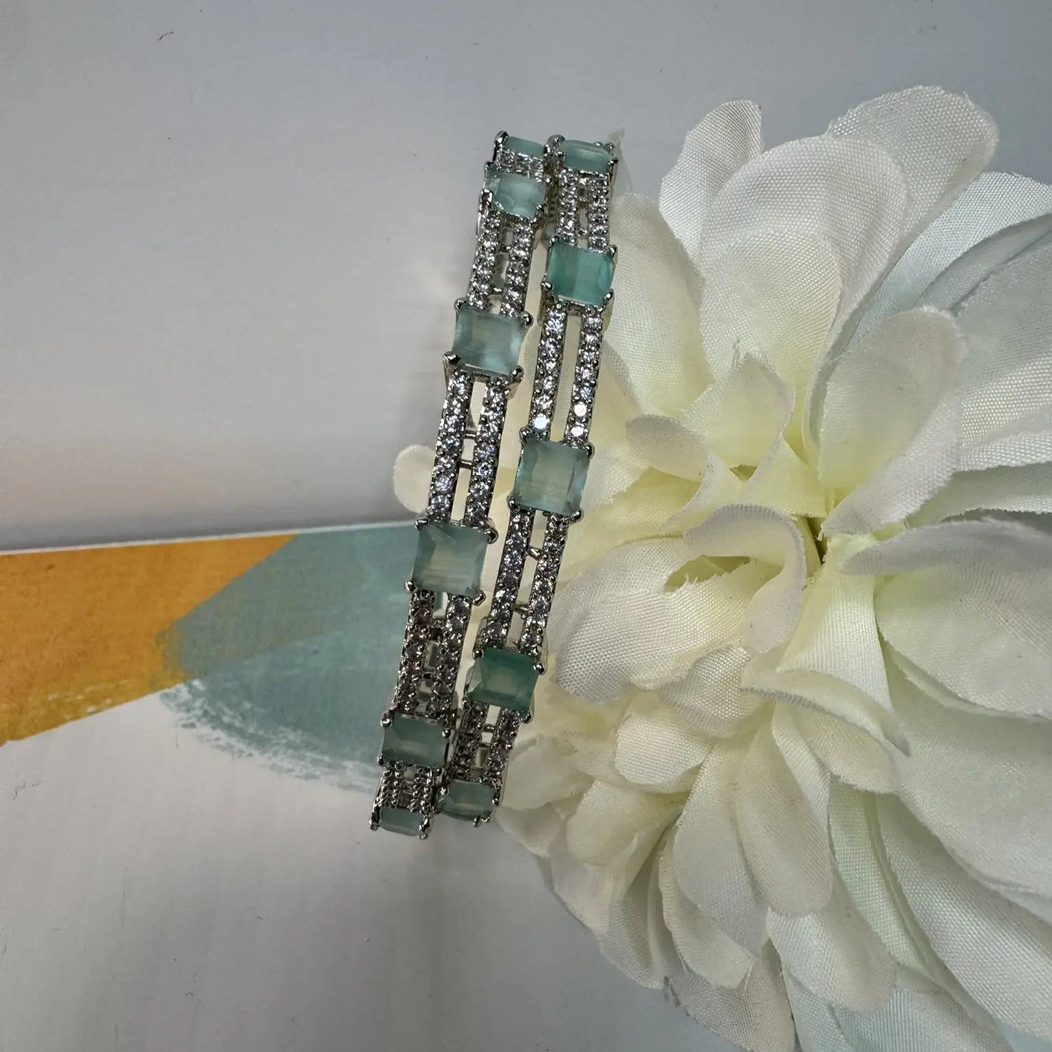 Two silver bangles with teal gemstones on a white flower