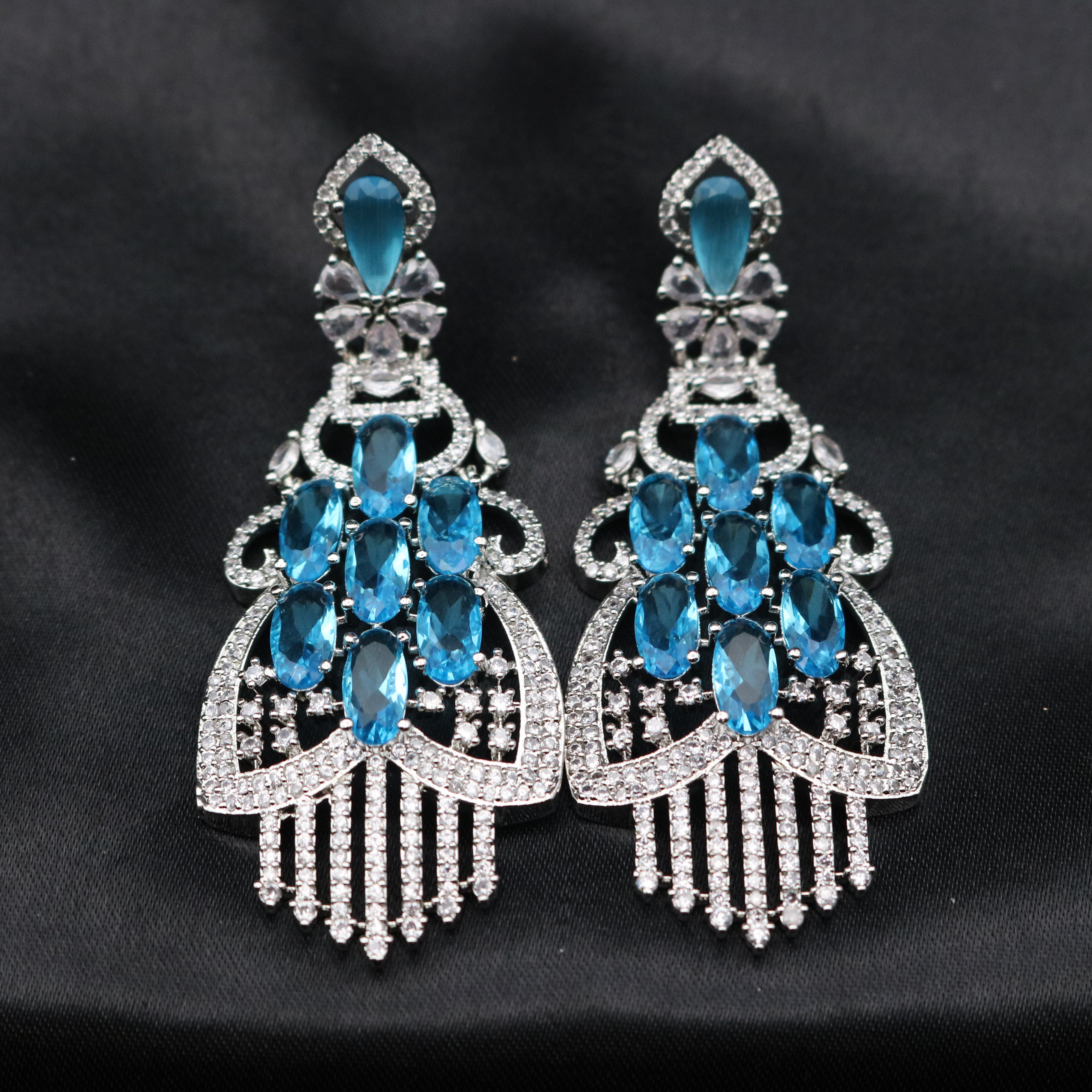 A pair of stainless steel earrings with sparkling blue American diamonds, arranged in a unique geometric pattern, set against a black background.