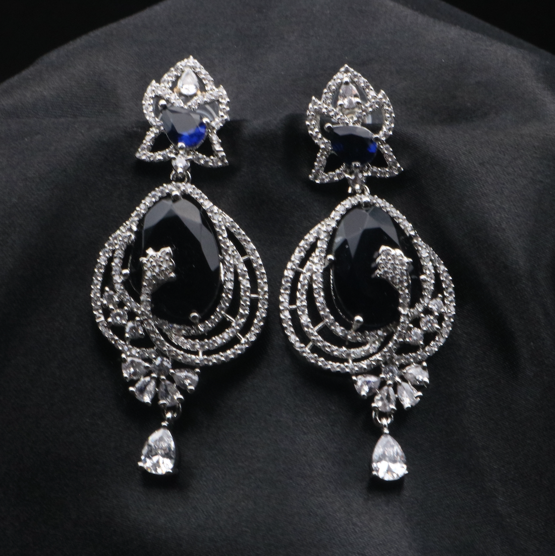 A pair of stainless steel earrings with blue and clear embellishments, designed to resemble a flower or a geometric shape, set with American diamonds.