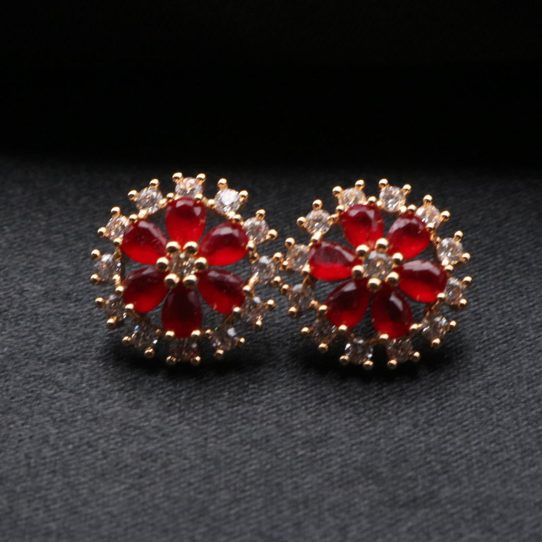 A pair of earrings featuring red gemstones surrounded by gold plating and small clear crystals, part of the PARIS collection.