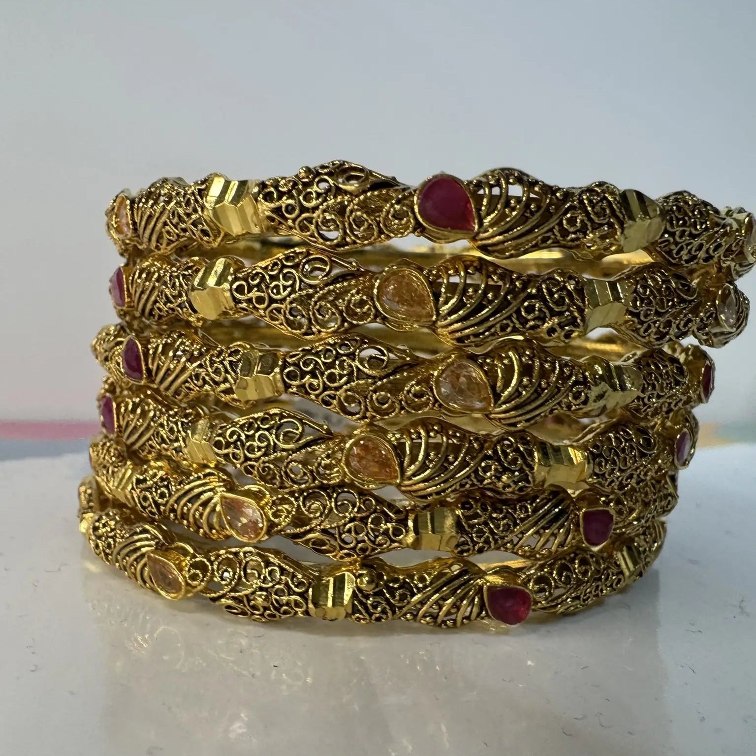 gold-plated bangles with red and champagne embellishments in an intricate design on a white surface