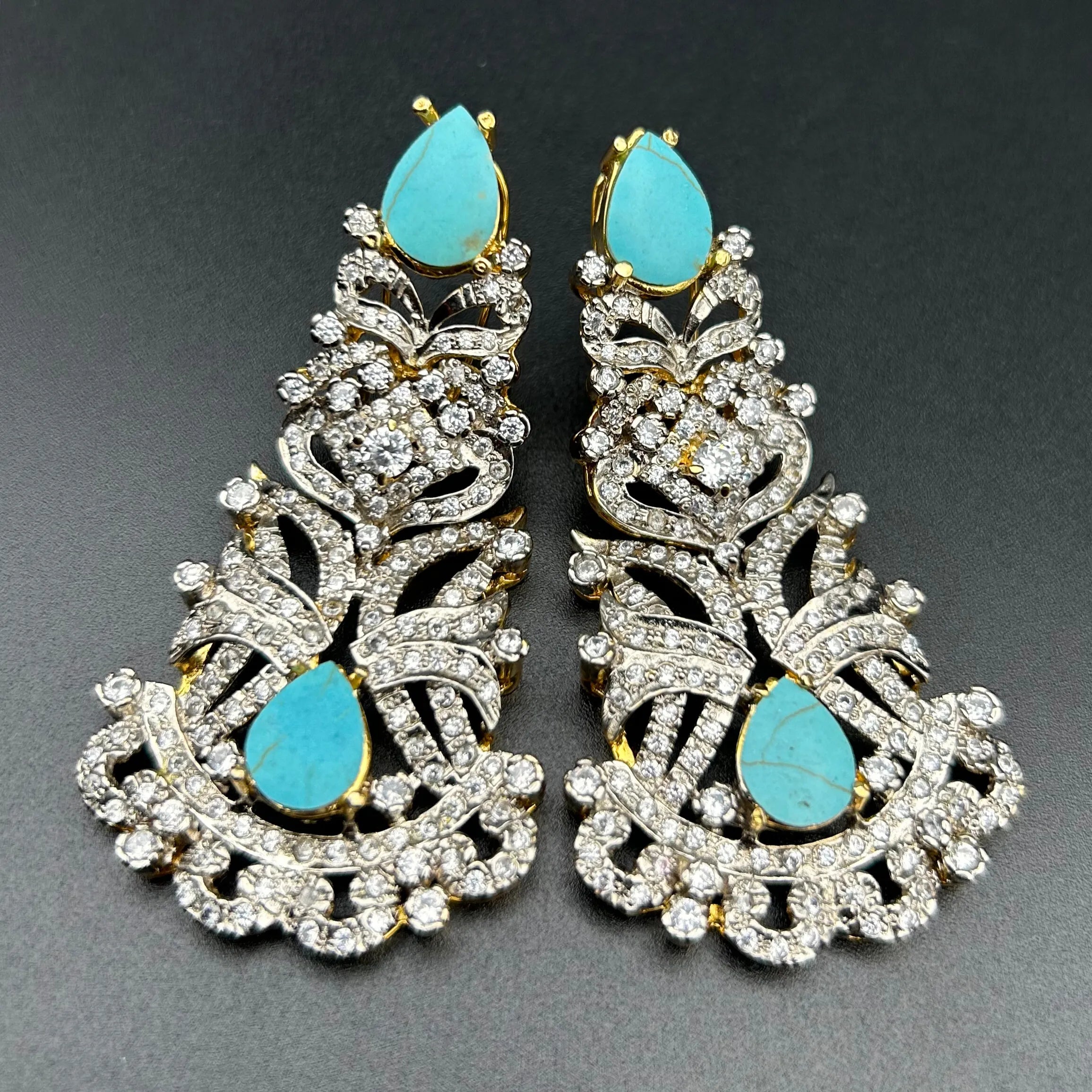 Pair of ornate earrings with turquoise stones on a dark background