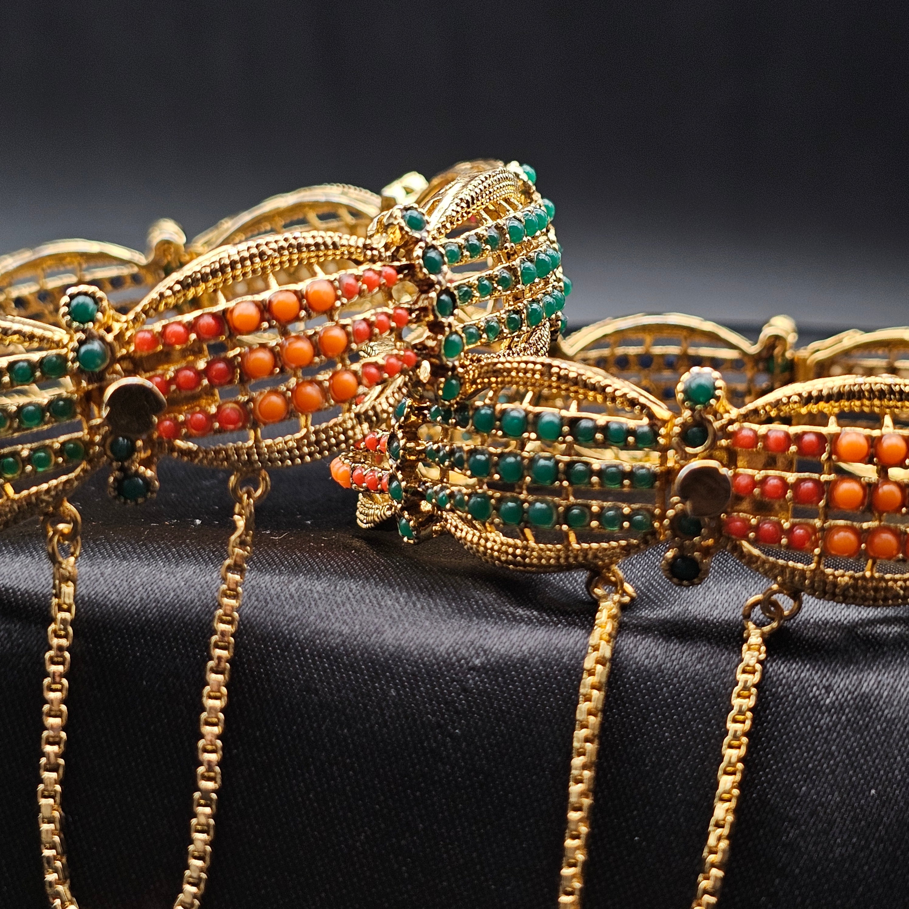 An array of gold-colored metal bangles adorned with multicolored beads displayed against a dark background.