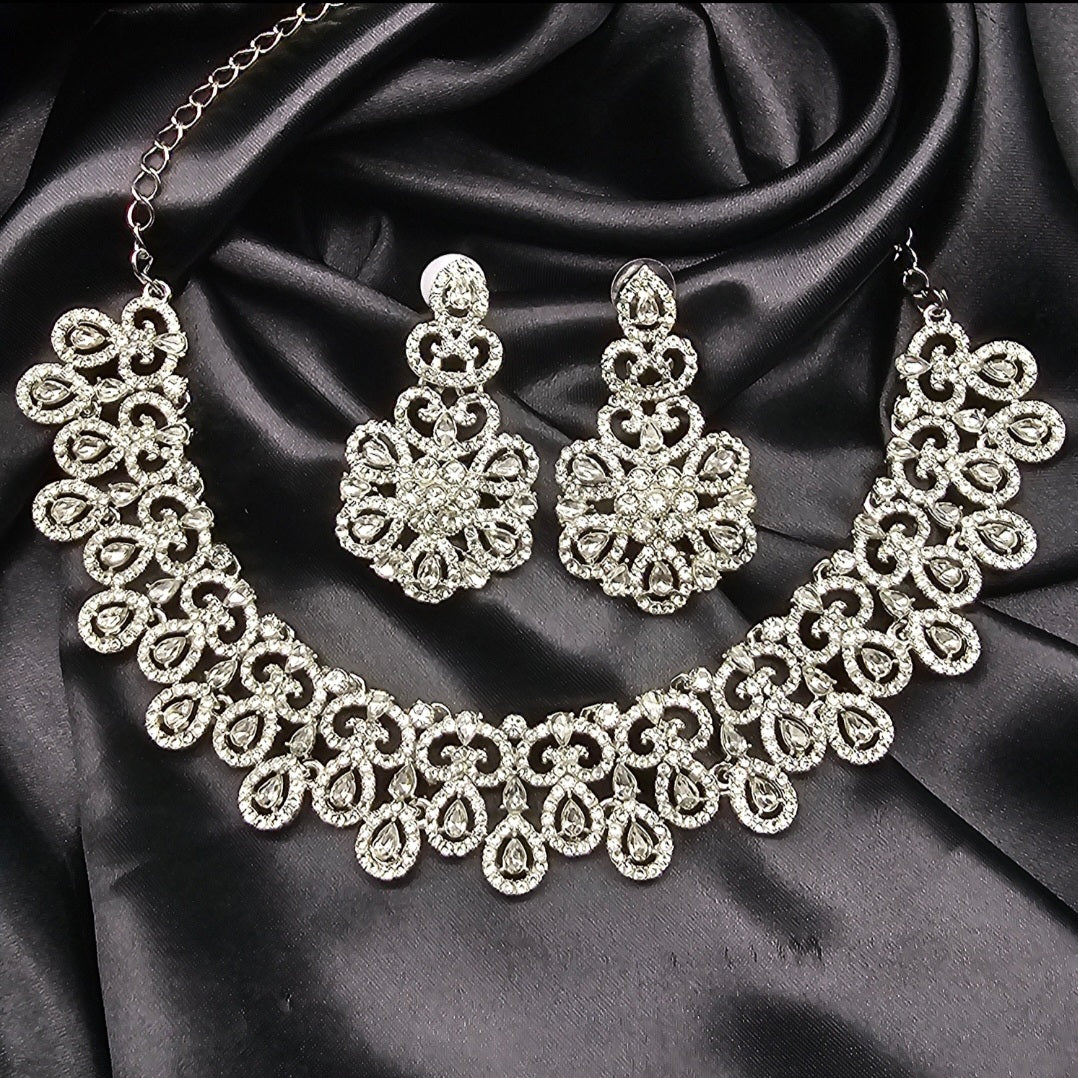 A silver necklace set with intricate design, displayed against a black background.