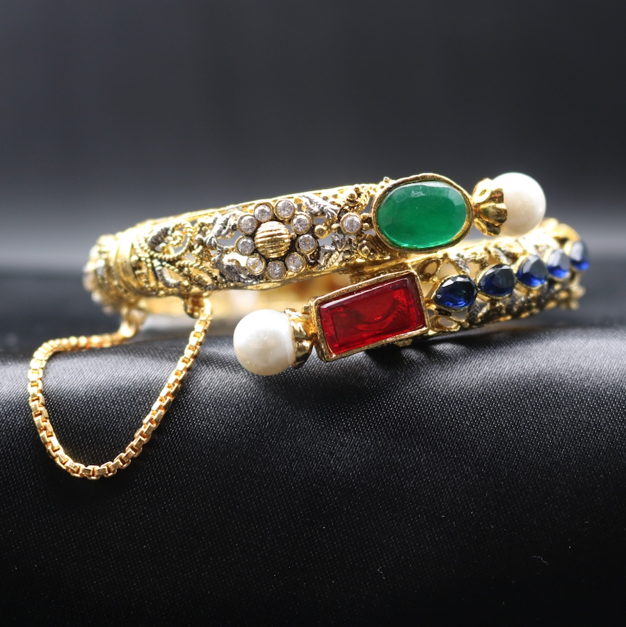 A gold-plated snake-shaped bangle bracelet adorned with multicolored gemstones and American diamonds, featuring a chain detail.