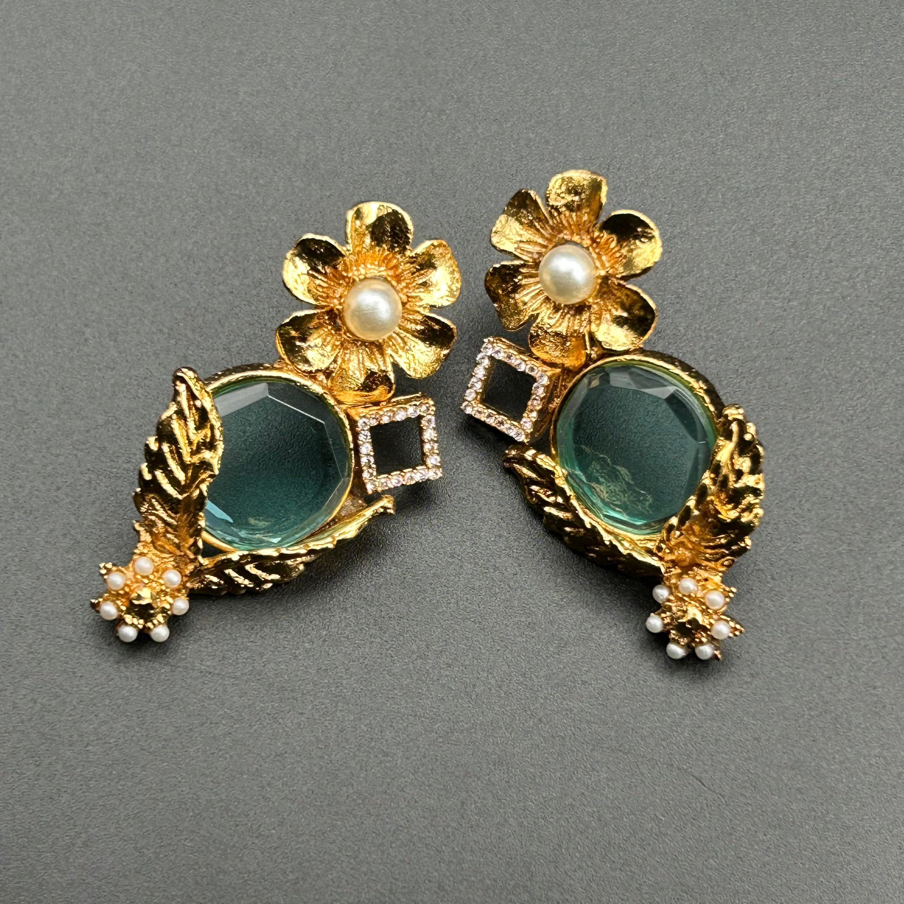 A pair of floral-shaped earrings with blue colored tints and gold plated designs.