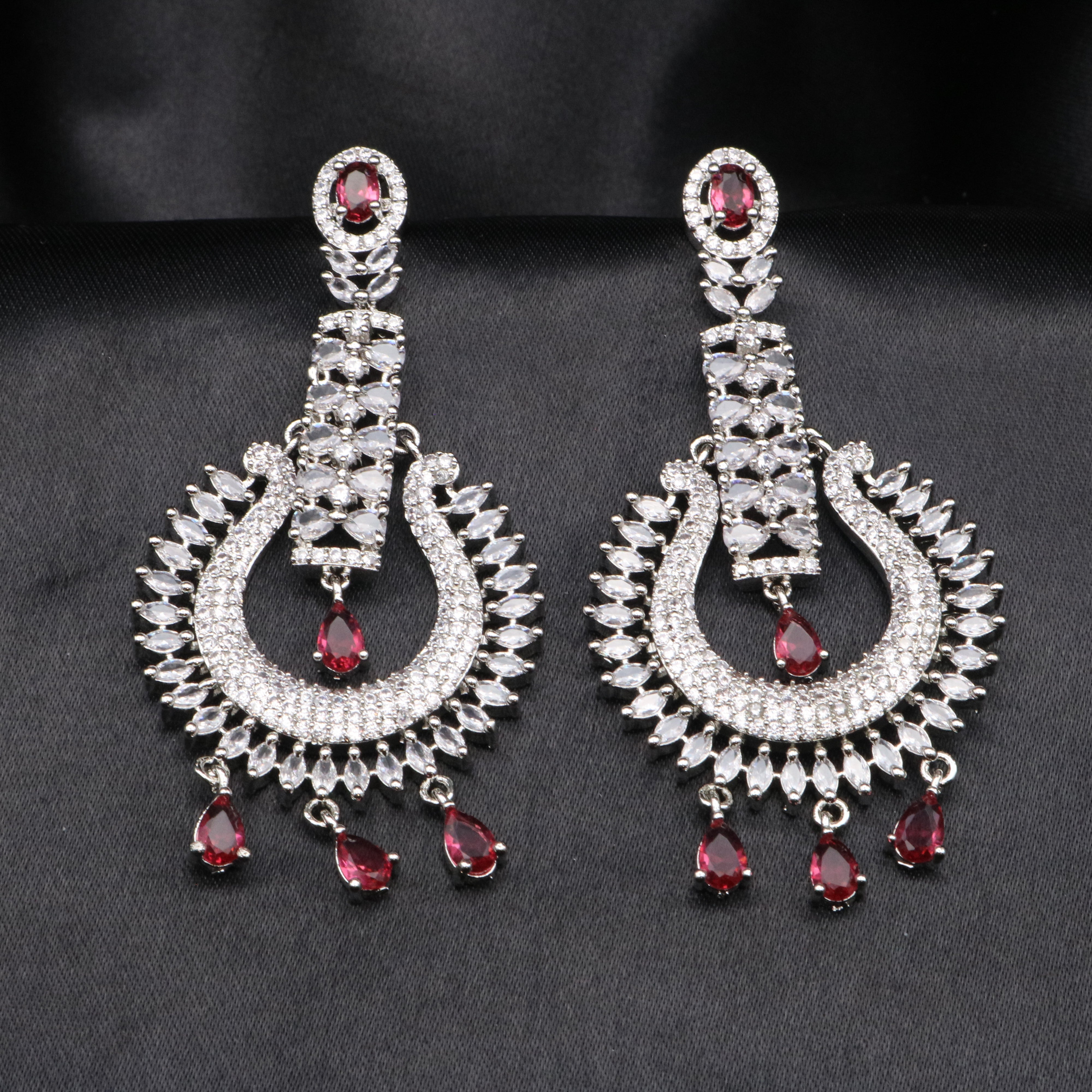 A pair of silver American diamond earrings featuring a geometric shaped design with hotpink and clear gemstones, and intricate details.