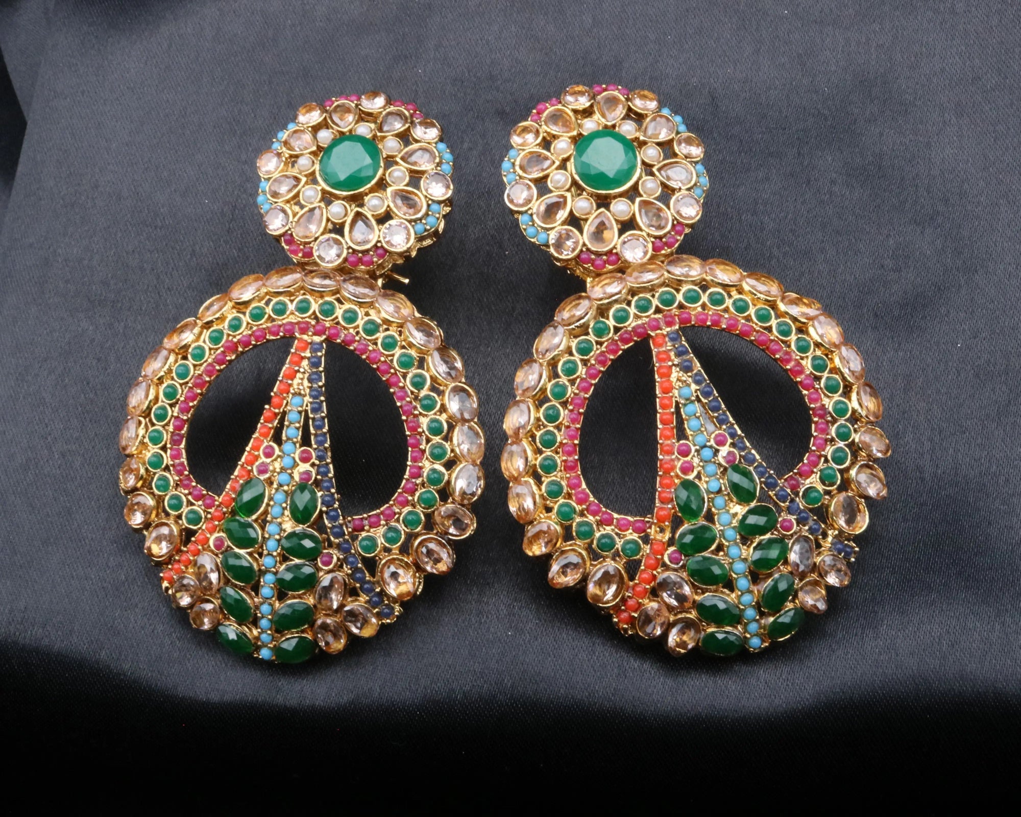 Ornate earrings with green and pink stones on a black background