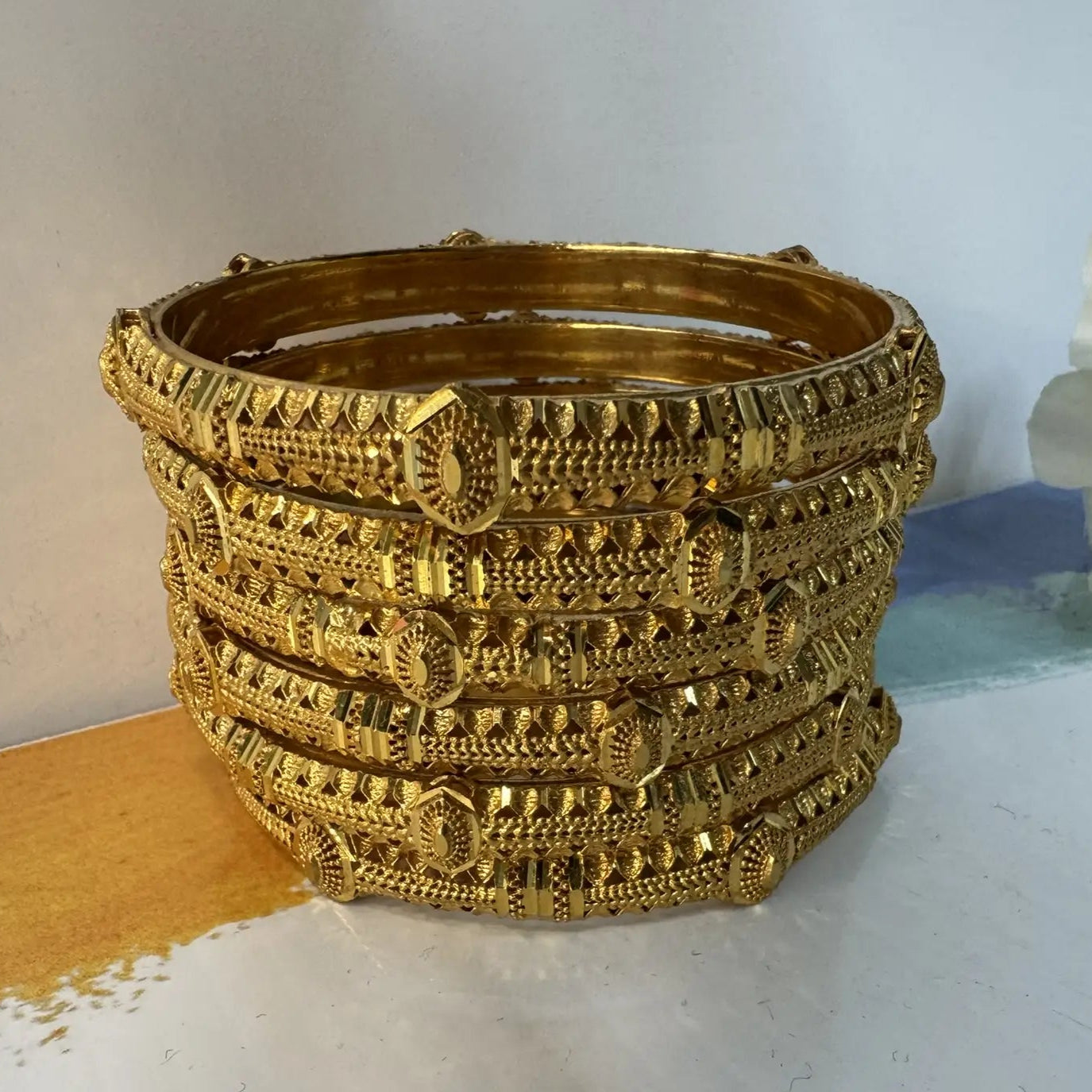 Stack of gold bangles on a white surface with a light blue background