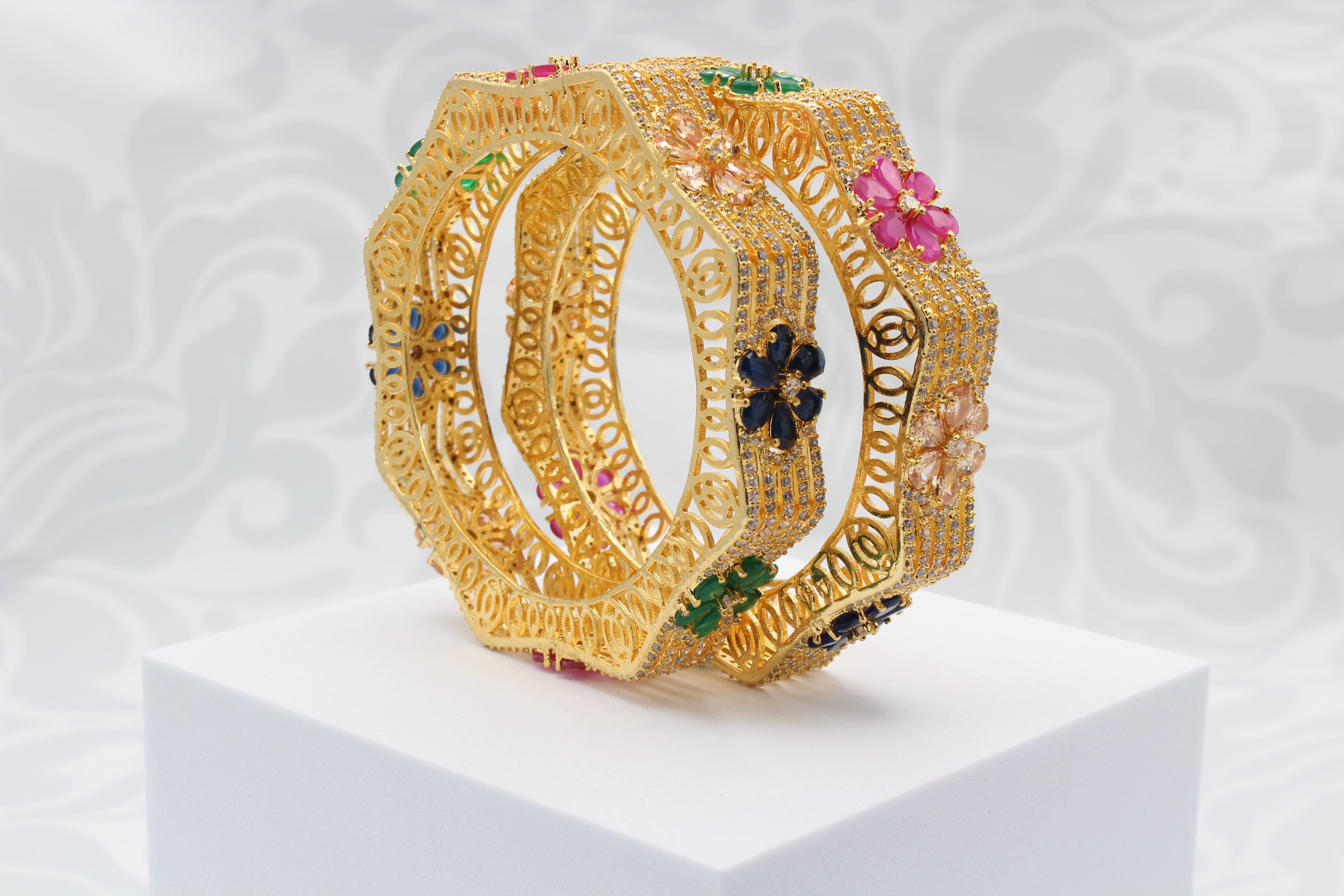 upright positioned gold-plated bangles with multicolor gemstones in a hexagonal design on white surface