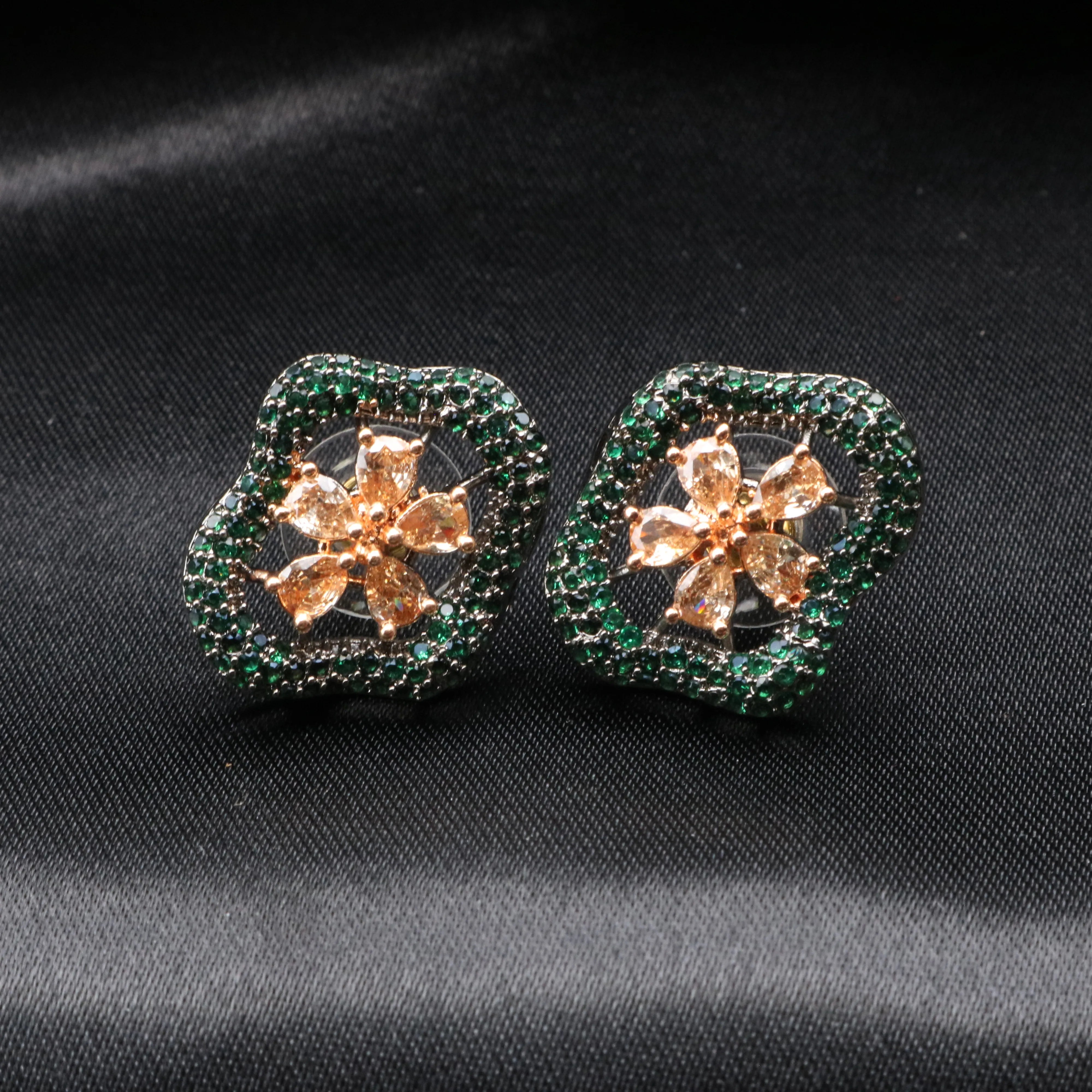 Pair of floral earrings with green and gold details on a black fabric background