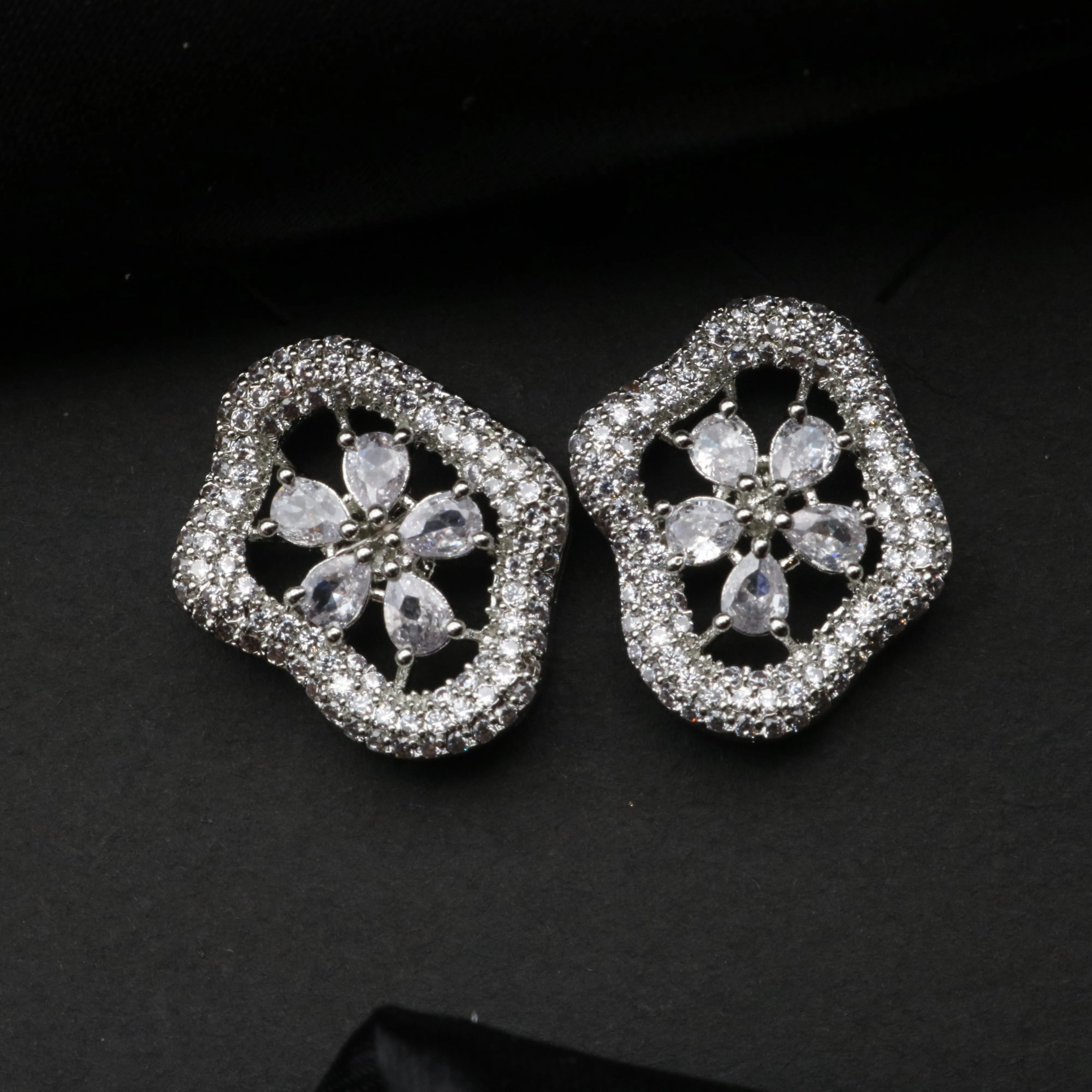 Pair of silver floral earrings with clear stones on a black background