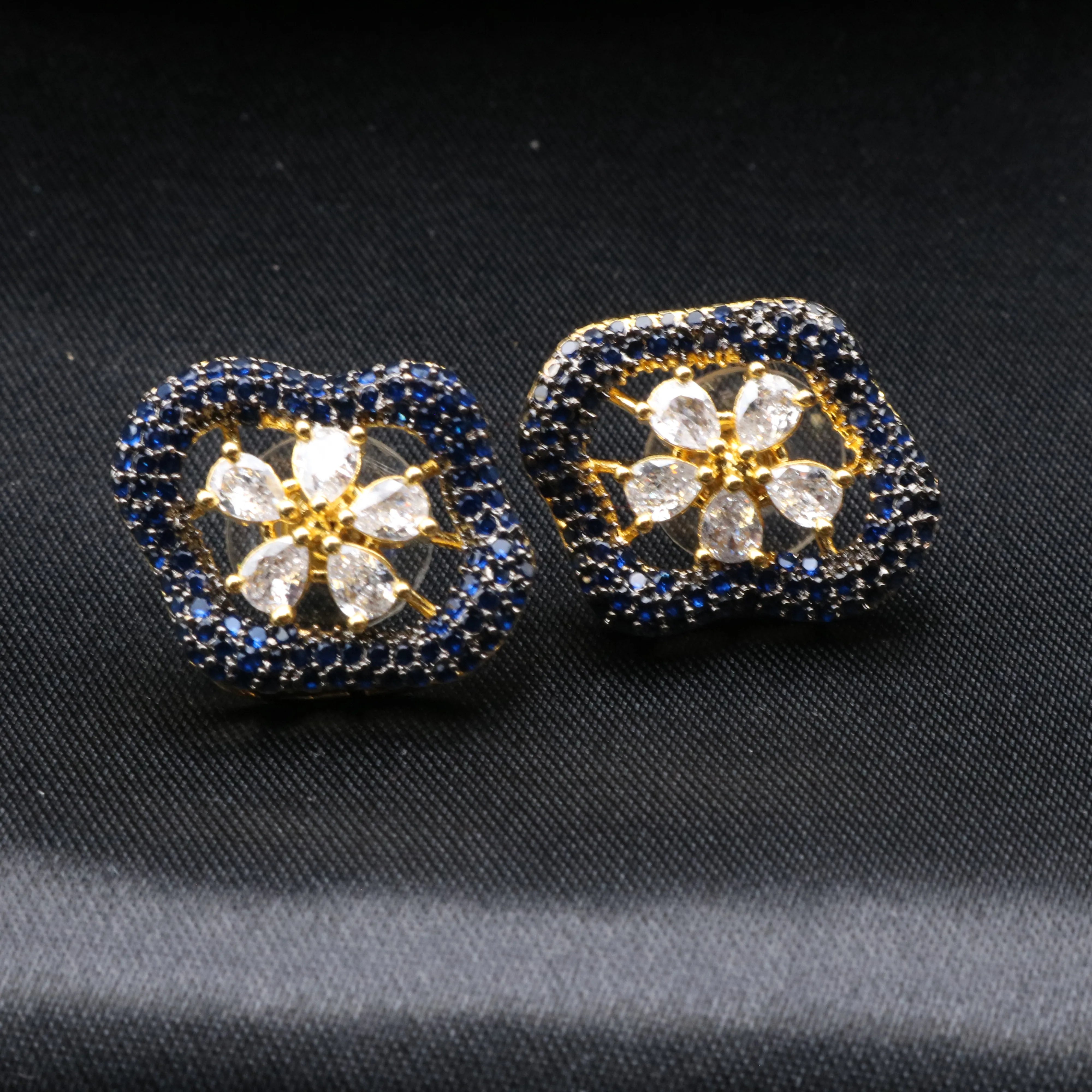 Pair of floral earrings with blue and gold accents on a black background