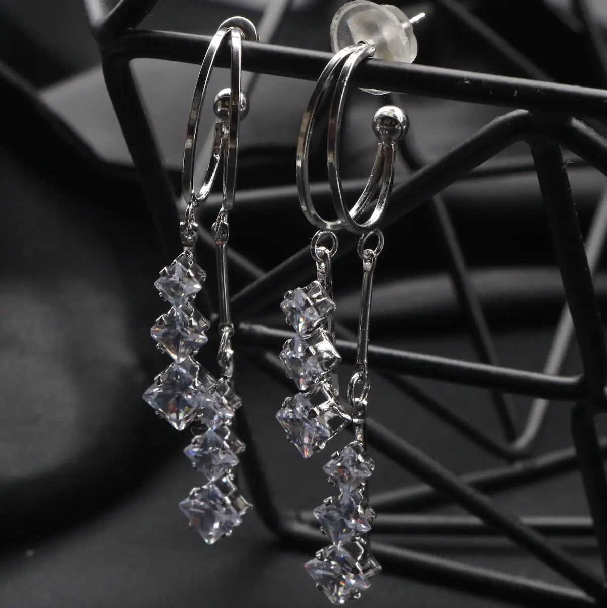 Silver stainless steel earrings with clear gemstones on a black metal stand.