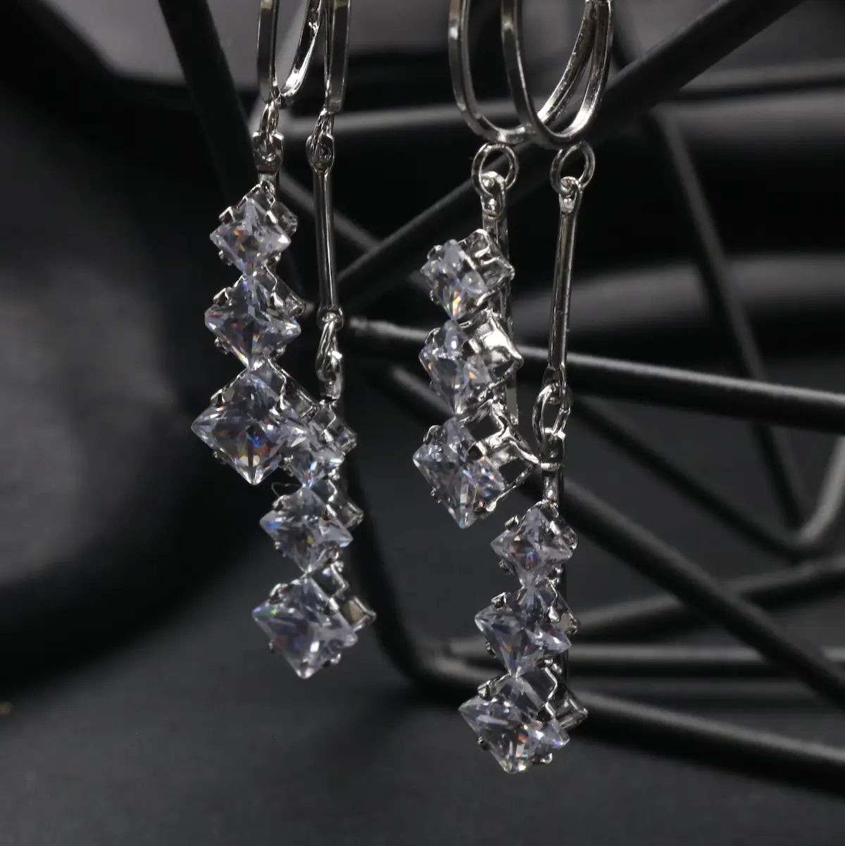 another angle of Silver stainless steel earrings with clear gemstones on a black metal stand.