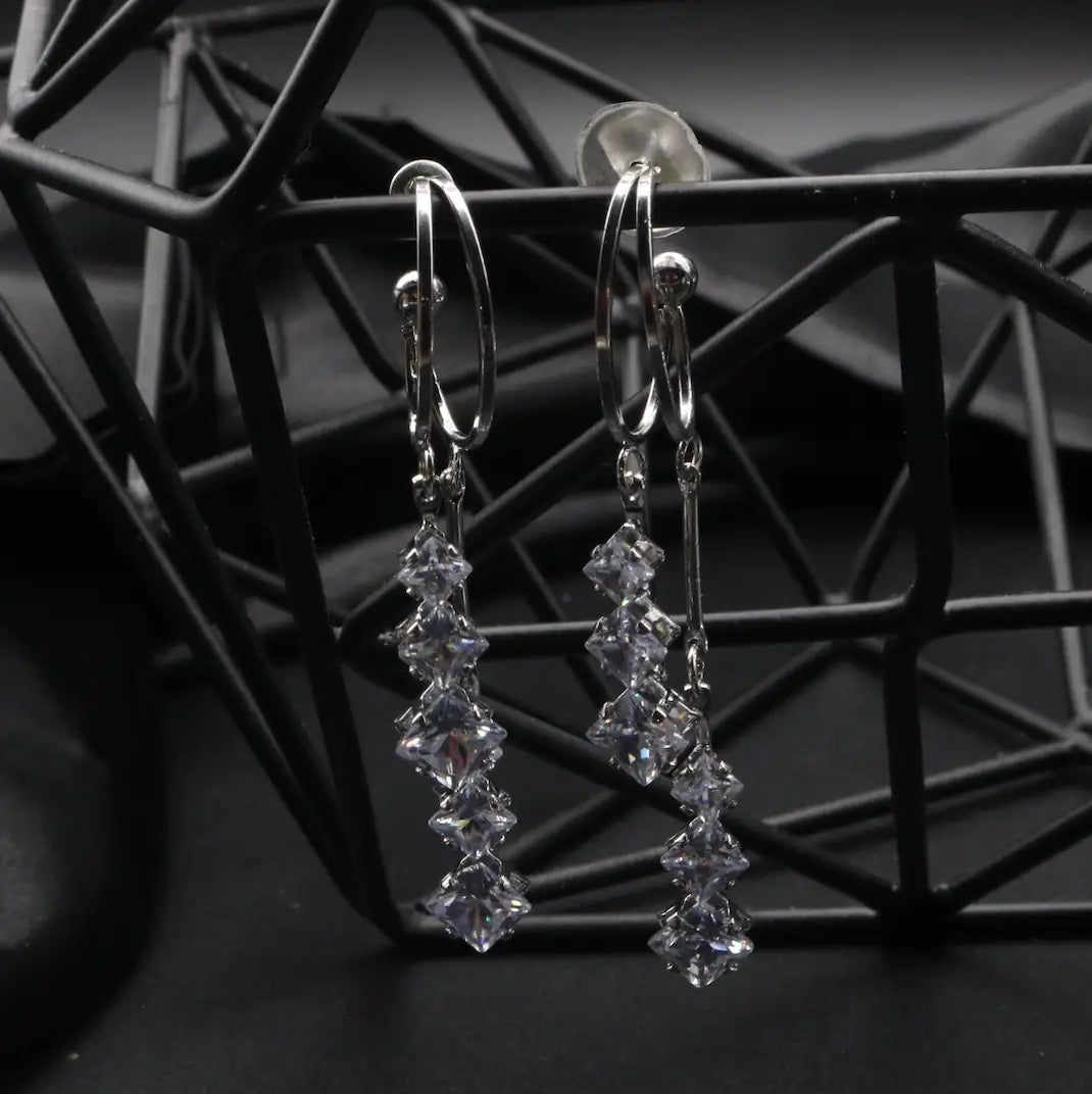 top angle of silver stainless steel earrings with clear gemstones on a black metal stand.