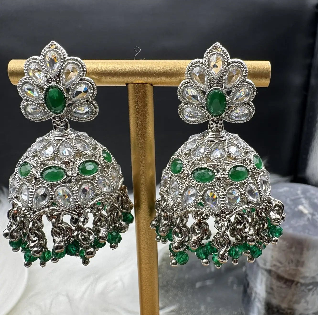 Pair of Pakistani style silver jhumka earrings with green gemstones on a gold stand.