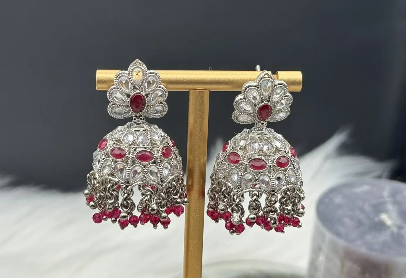 top view of pair of Pakistani style silver jhumka earrings with red gemstones on a gold stand.