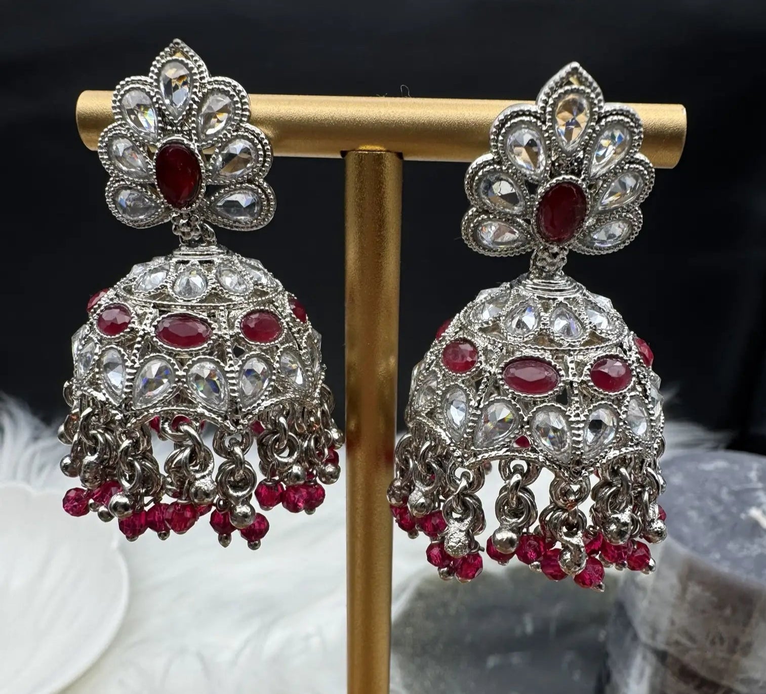 Pair of Pakistani style silver jhumka earrings with red gemstones on a gold stand.