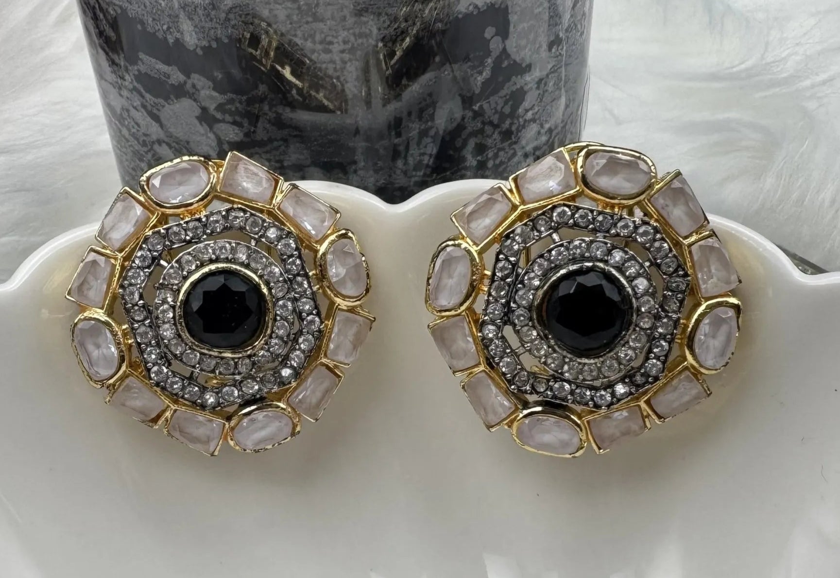 Pair of gold-plated and American diamonds earrings with black center stones and gold and silver accents on a white surface.