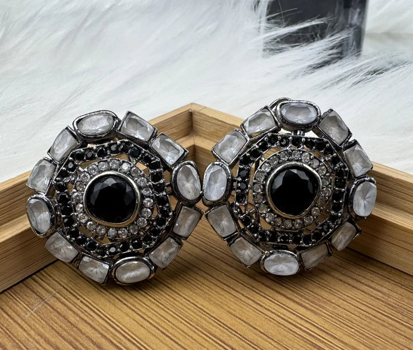 Pair of gold-plated and American diamonds earrings with black center and crystal-like stones on a wooden surface.