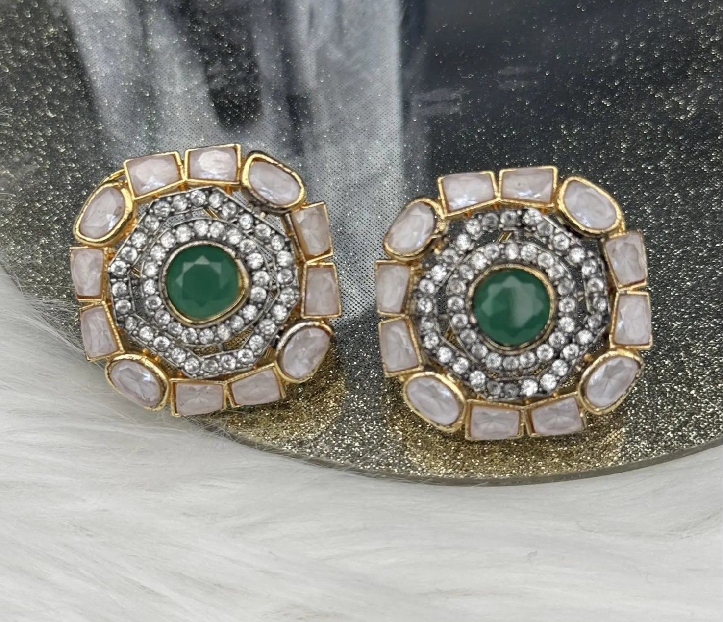 Pair of gold-plated and American diamonds earrings with green gemstones and gold accents on a reflective surface.