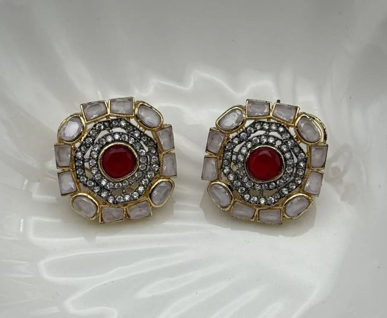 Pair of gold-plated and American diamonds earrings with red center and gold frame on a white dish.