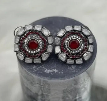 Pair of gold-plated and American diamonds earrings with red gemstones and silver accents on a cylindrical gray stand.