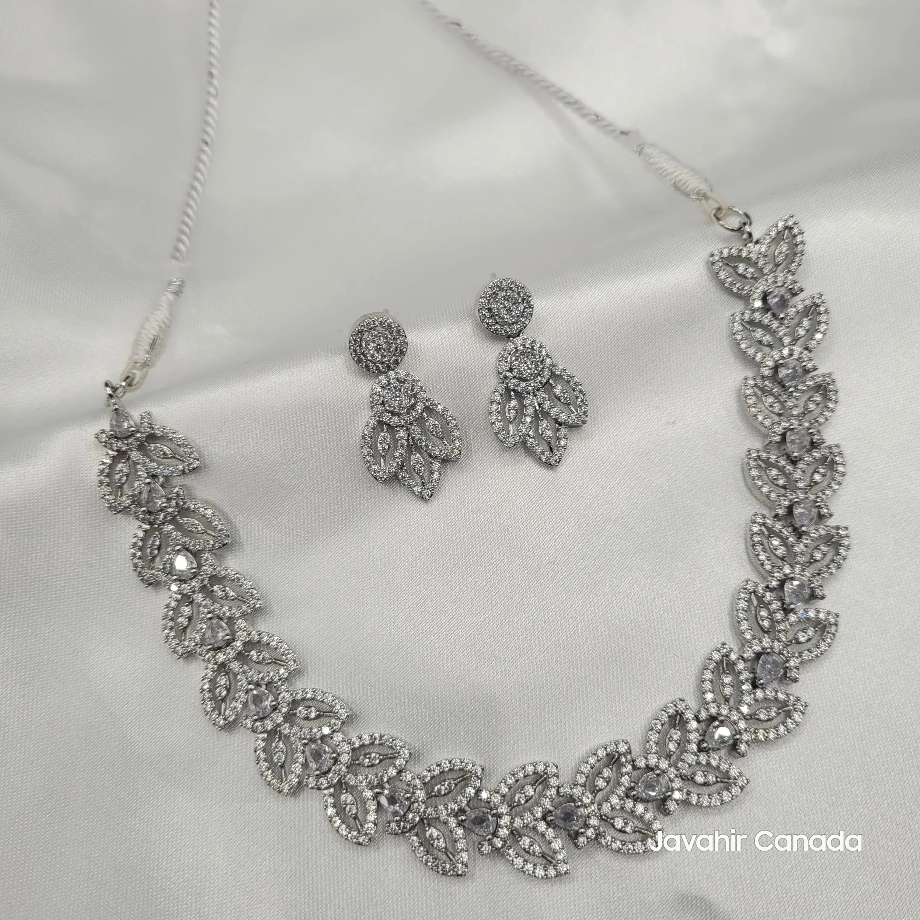 Top angle flat lay of the Aria necklace and earrings on a satin background.