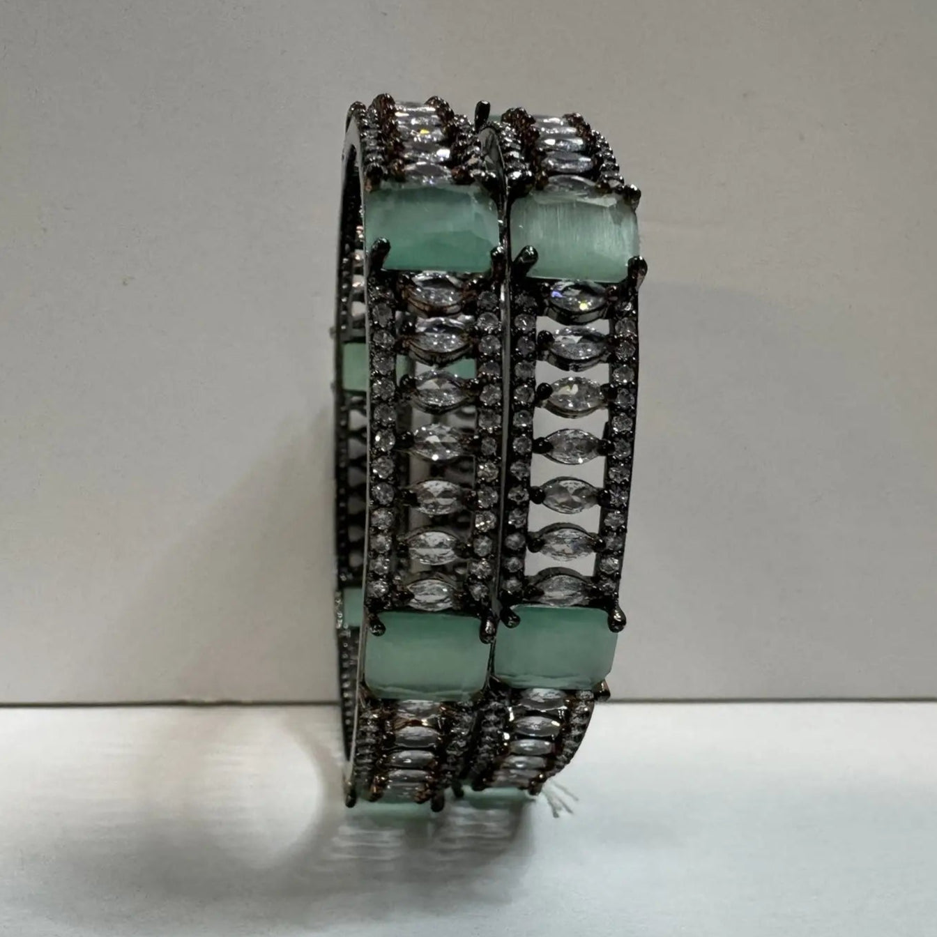 Pair of teal and clear gemstone bangles with silver accents on a light gray background