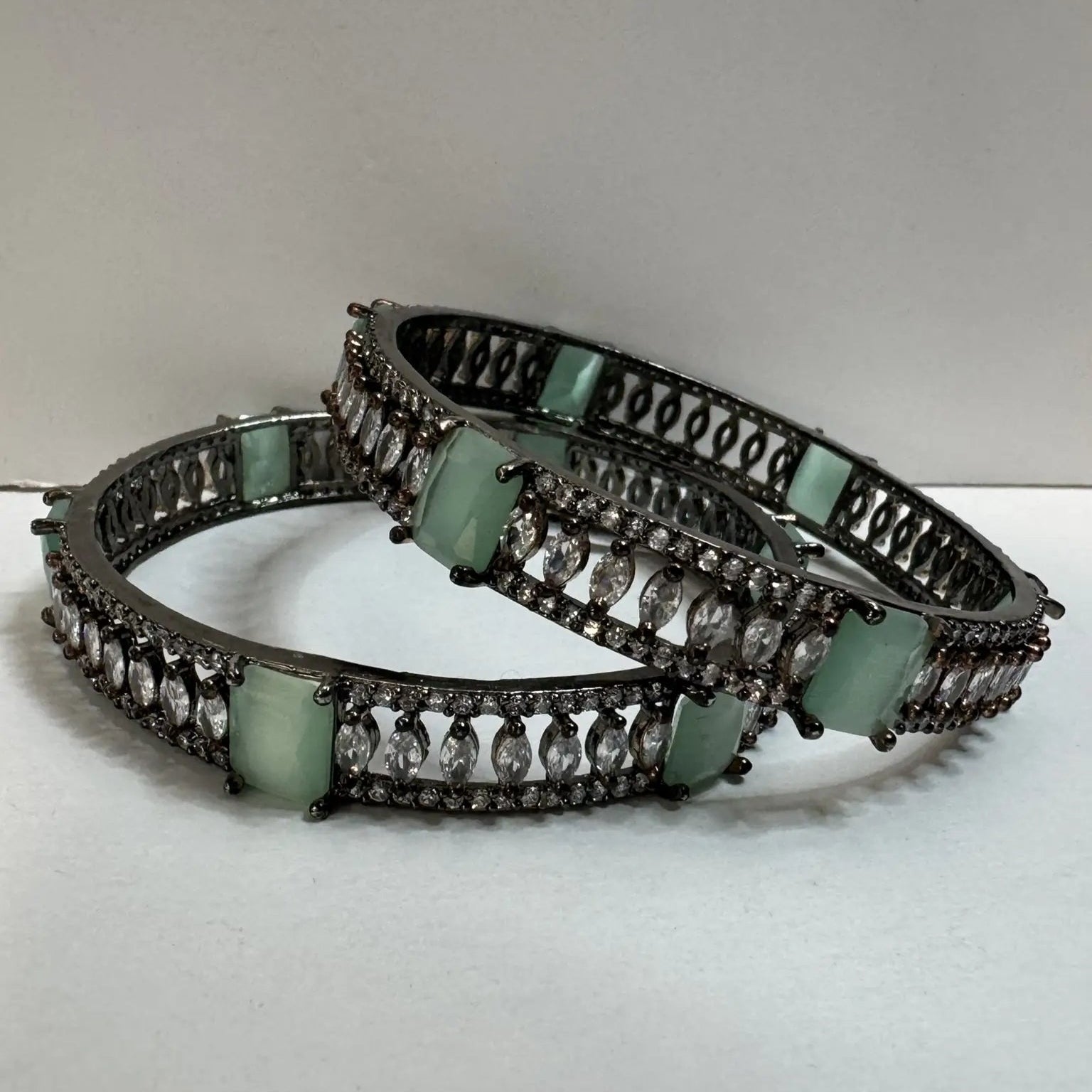 Bangles with teal and clear gemstones and stainless steel finish on a white background