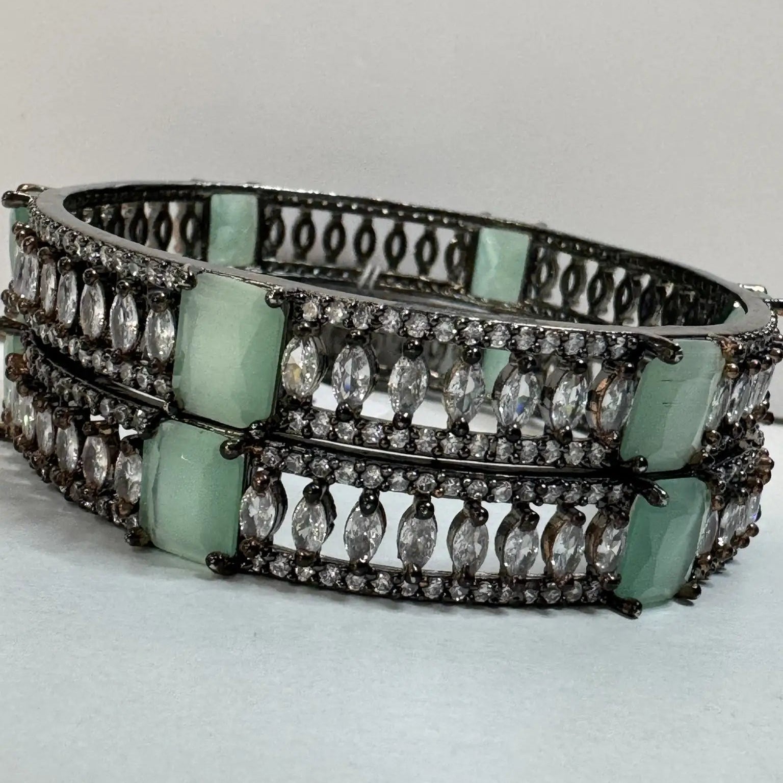 Multilayered bangles with teal and clear gemstones on a light gray background