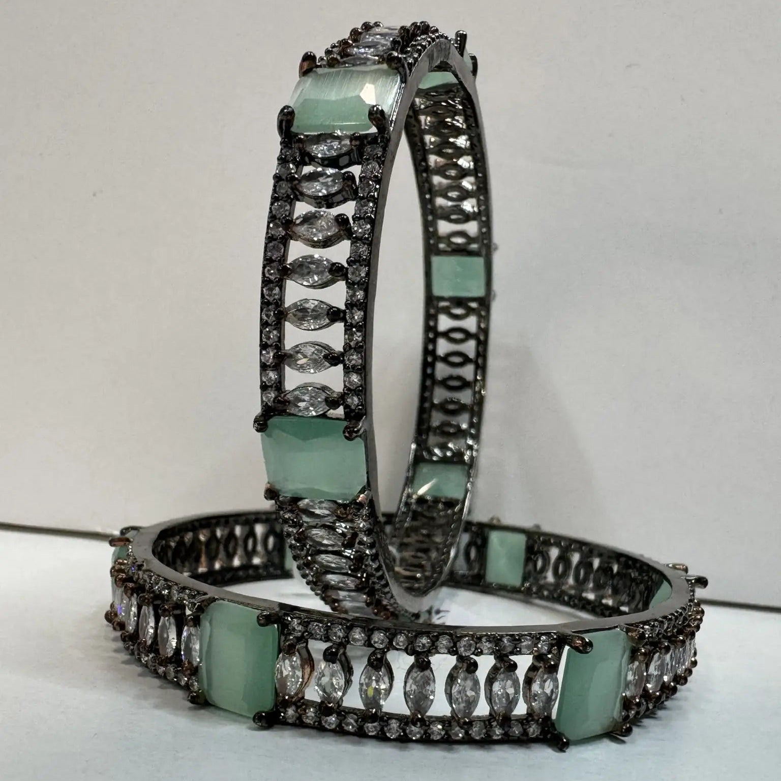 Pair of teal gemstone bangles with silver accents on a light gray background