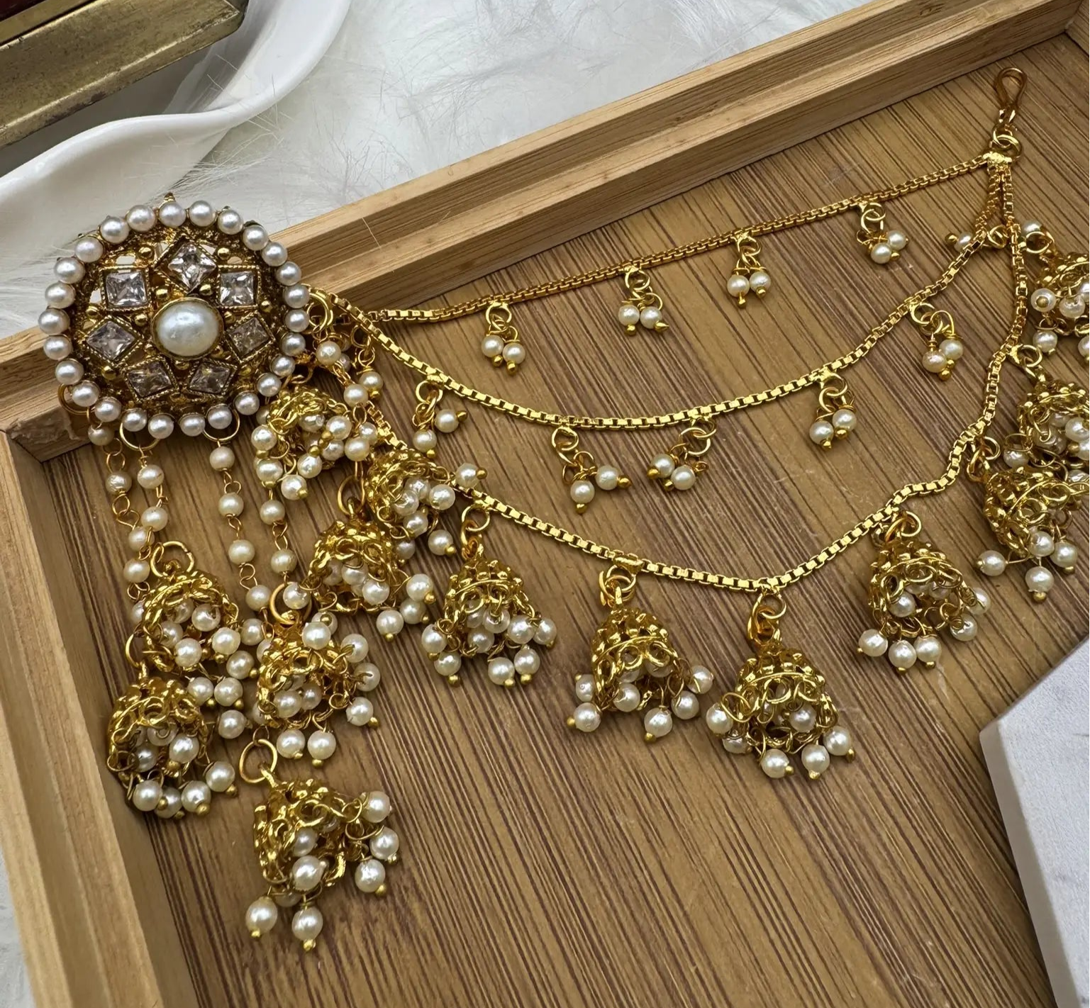 A pair of stainless steel and gold plated jhumka style earrings  with intricate saharas and hanging details, displayed on a wooden tray.