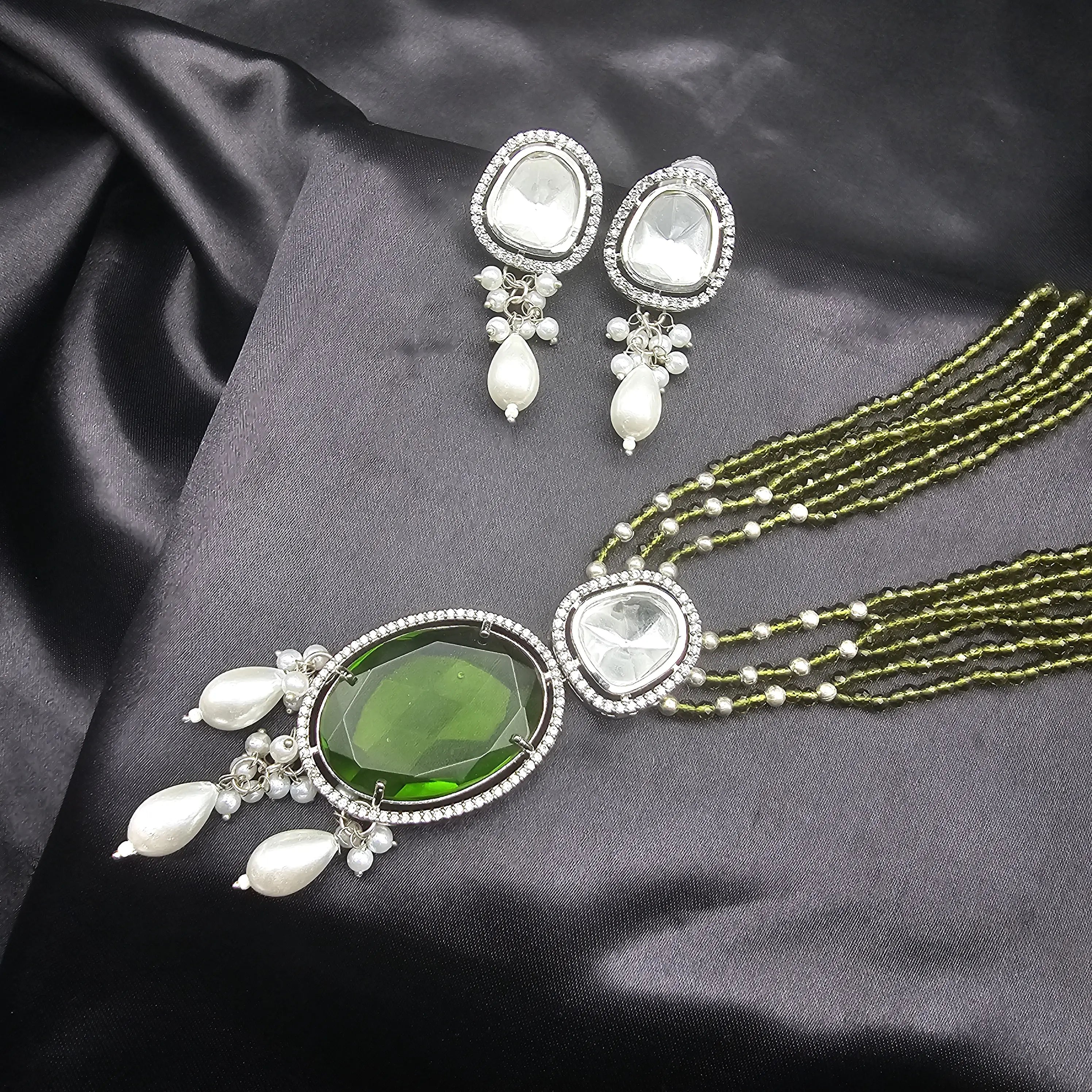 Caspian necklace set in olive green variant with large green center stone, pearl drops, and matching earrings on black fabric.