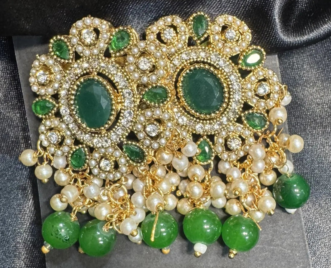 Earrings with green gemstones and gold accents on a black satin background