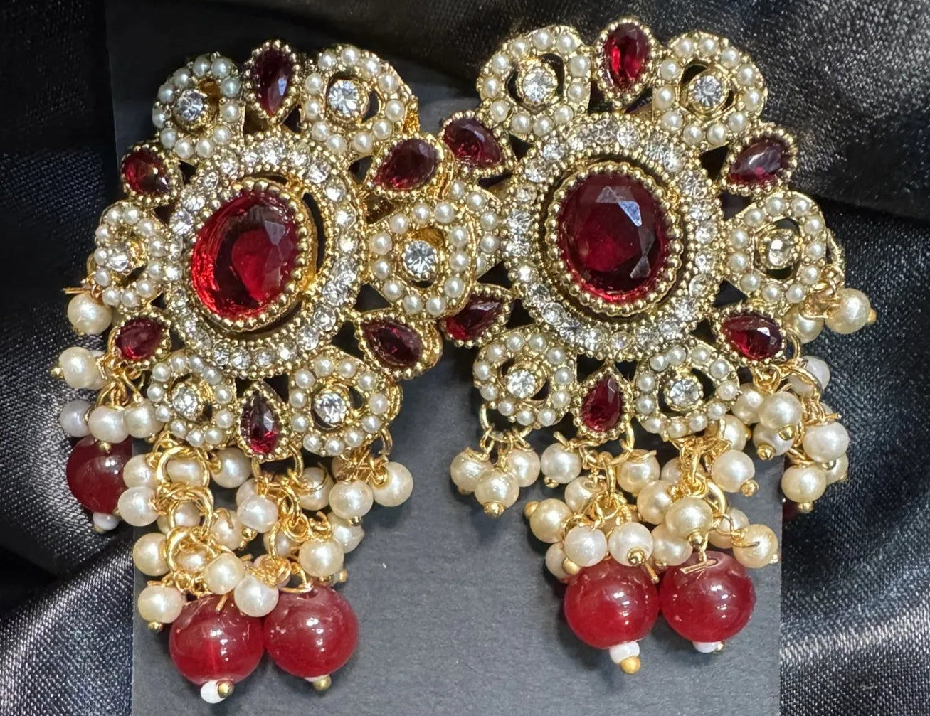 Ornate earrings with red gemstones and pearls on a dark fabric background