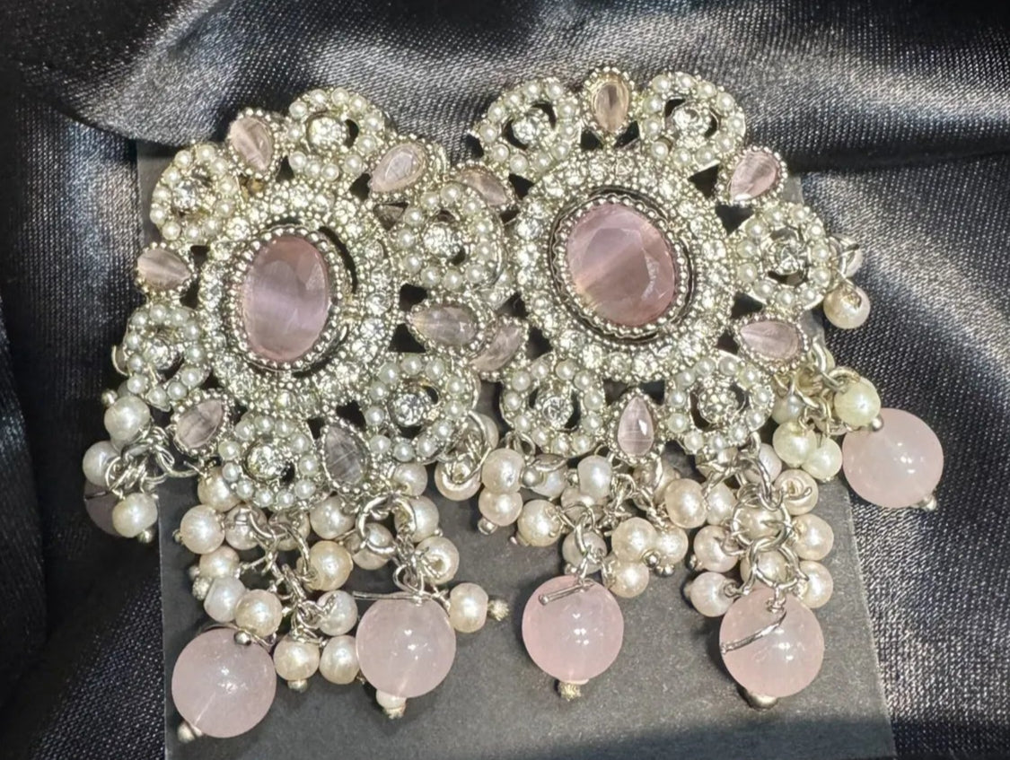 Ornate earrings with pink stones and pearls on a black satin background