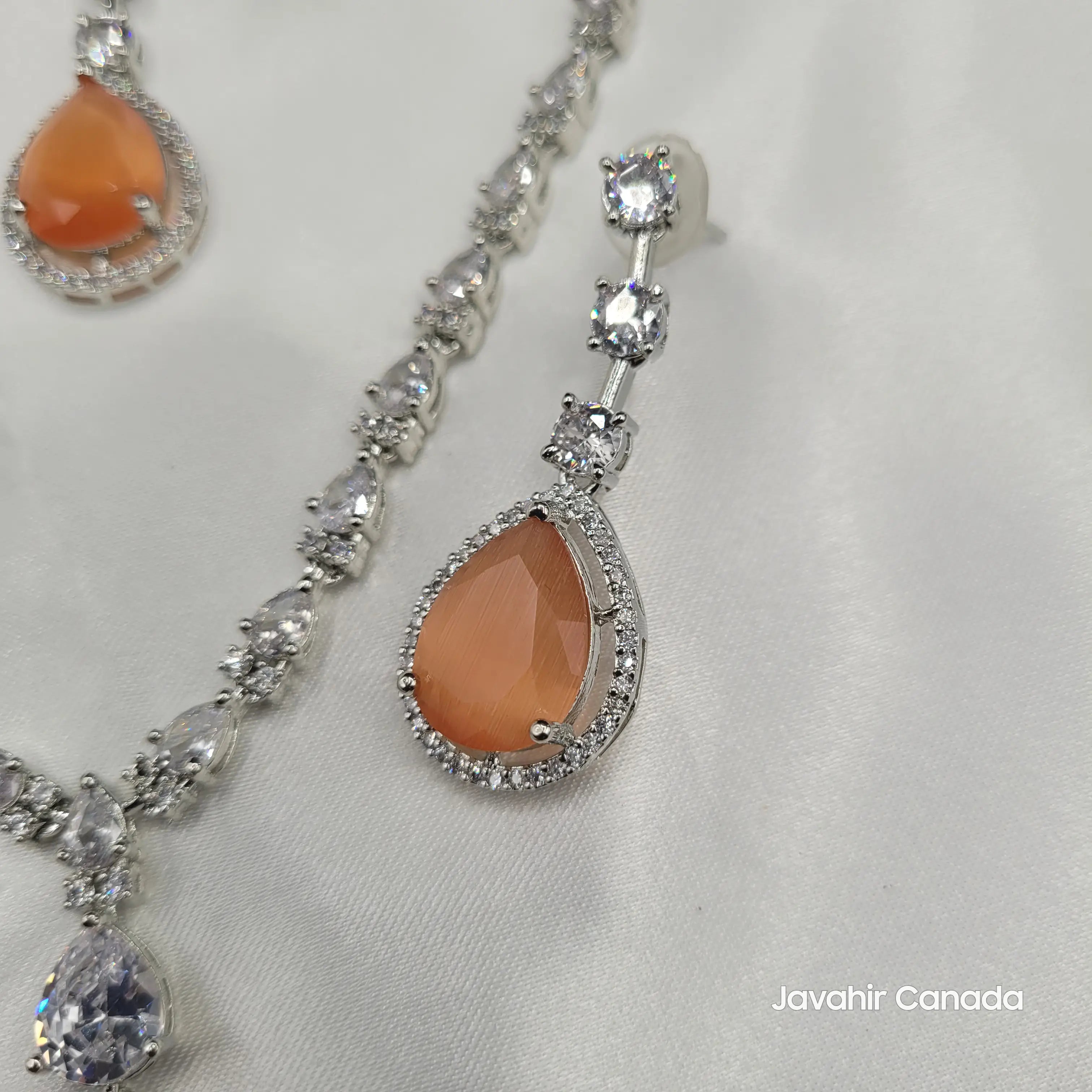 Close-up of orange teardrop gemstone earring bordered with CZ stones on a silver-tone chain.