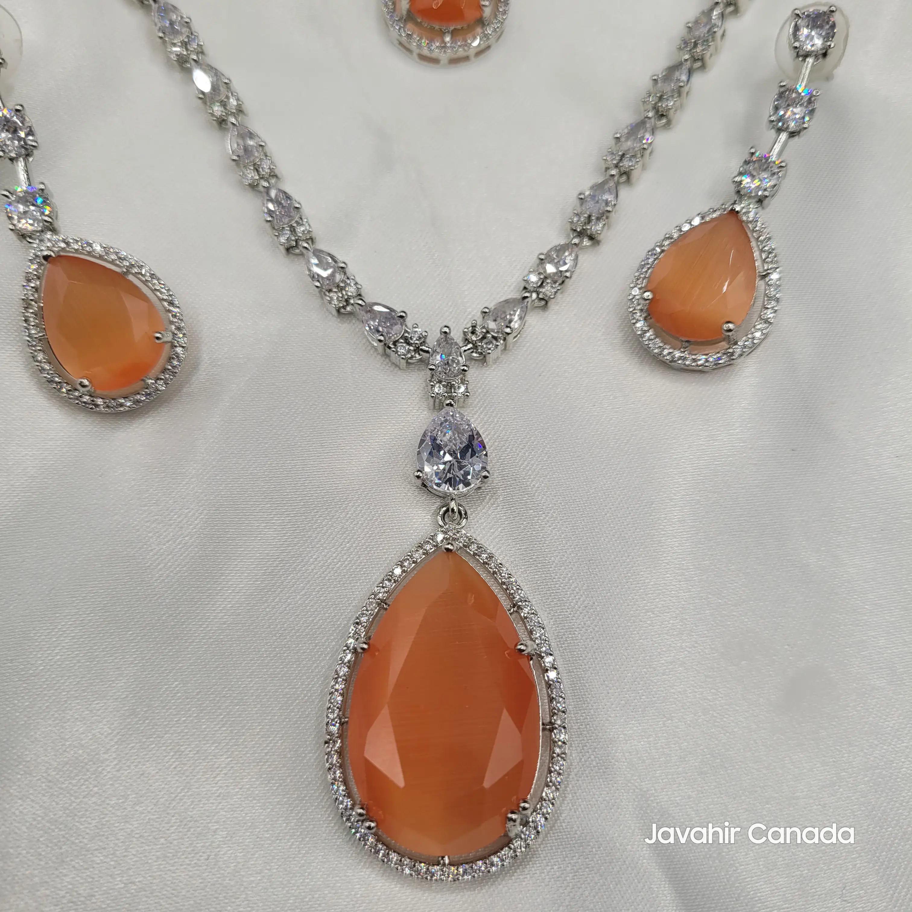 Necklace and earring set with orange teardrop centerpiece and CZ accents displayed on satin.