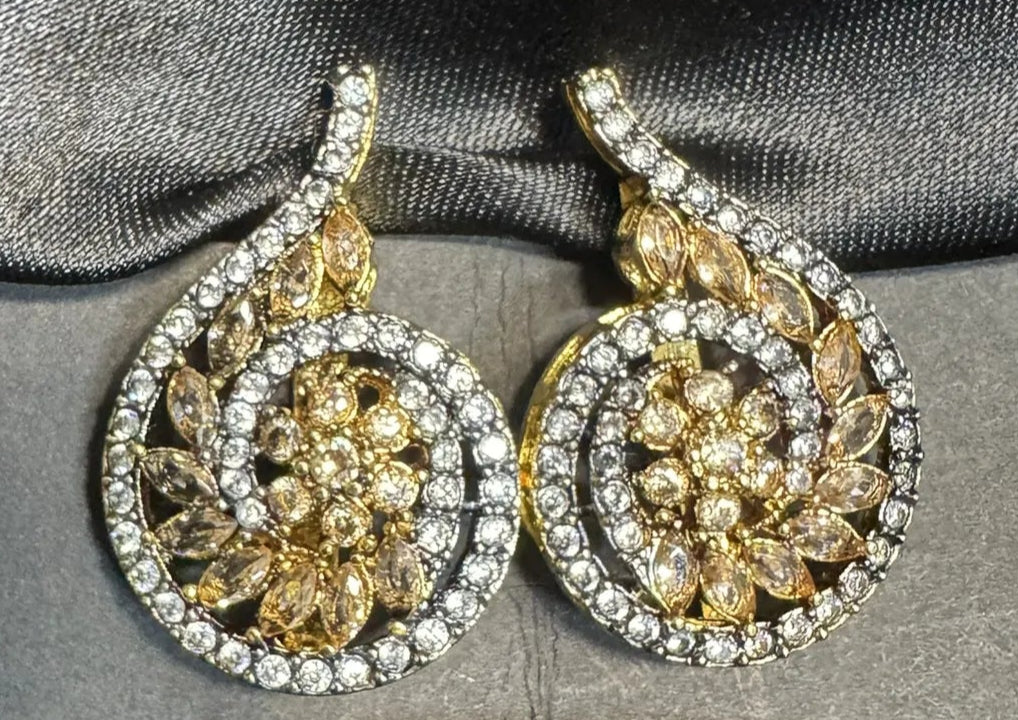 Pair of gold and American diamond earrings on a black satin surface