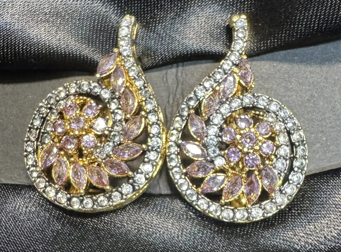 Pair of earrings with purple gemstones and gold accents on a black satin background
