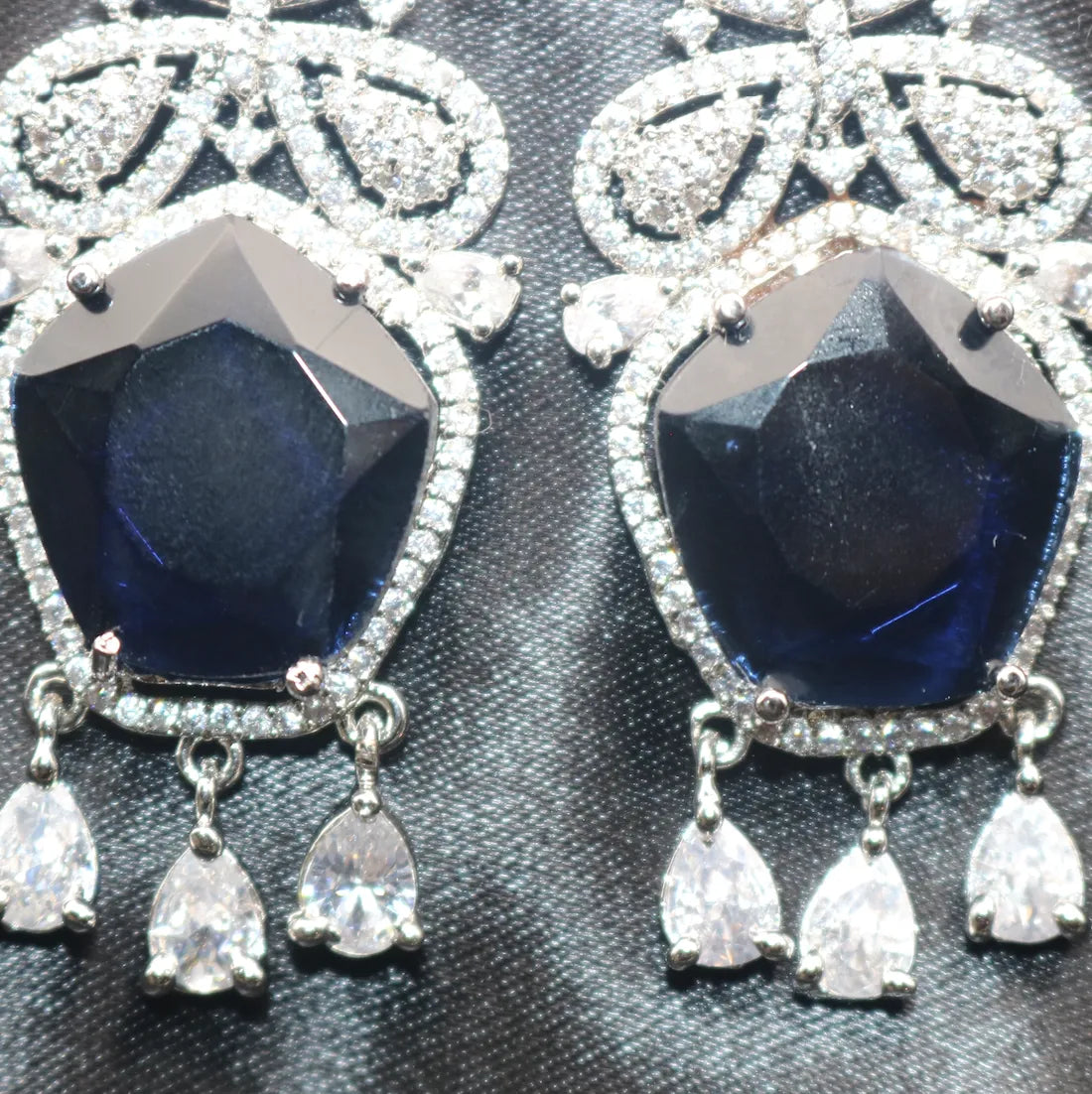 Pair of American diamonds earrings with blue gemstones and silver accents on a textured black background