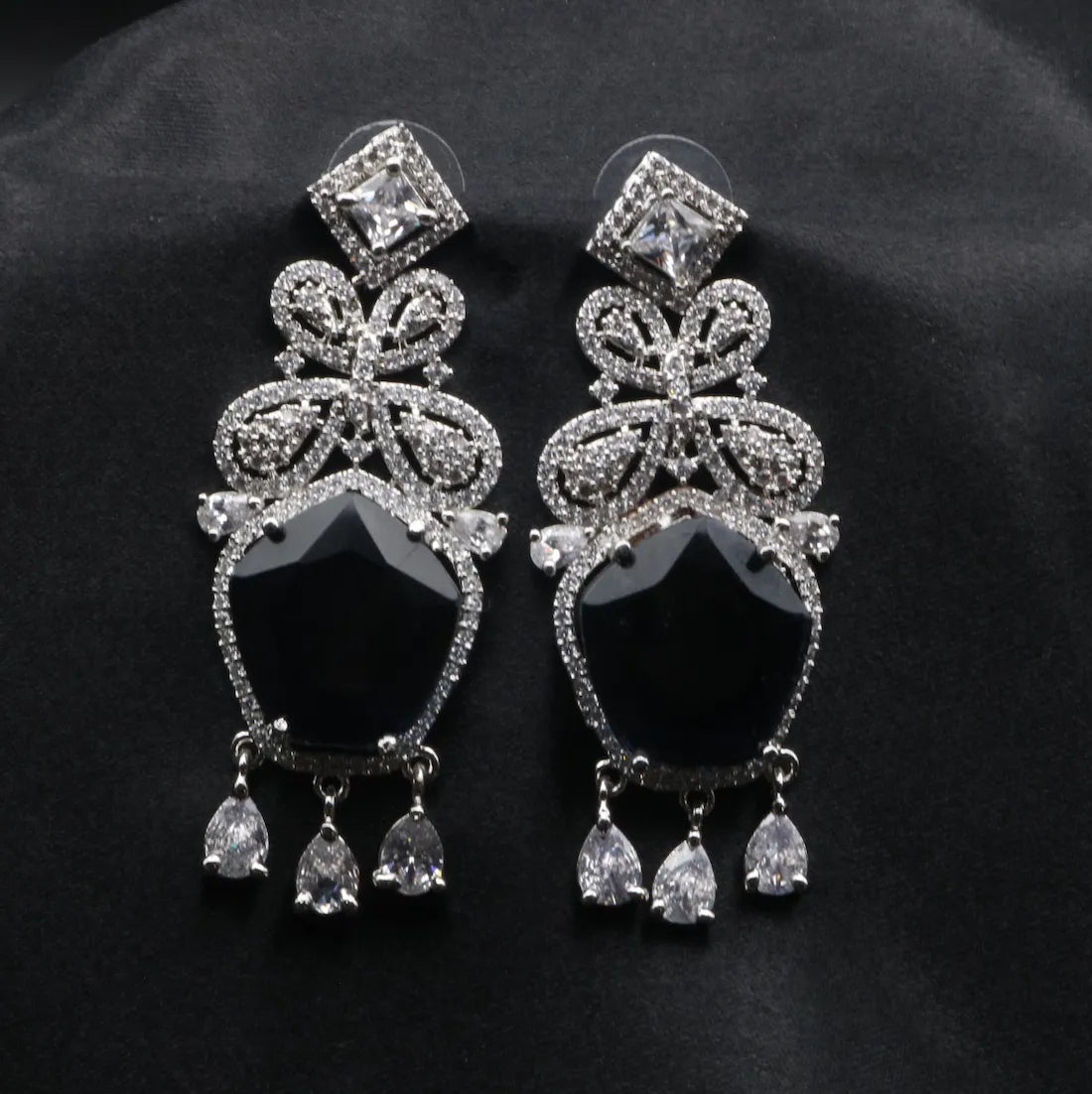 Pair of ornate silver American diamonds earrings with blue stones on a dark background