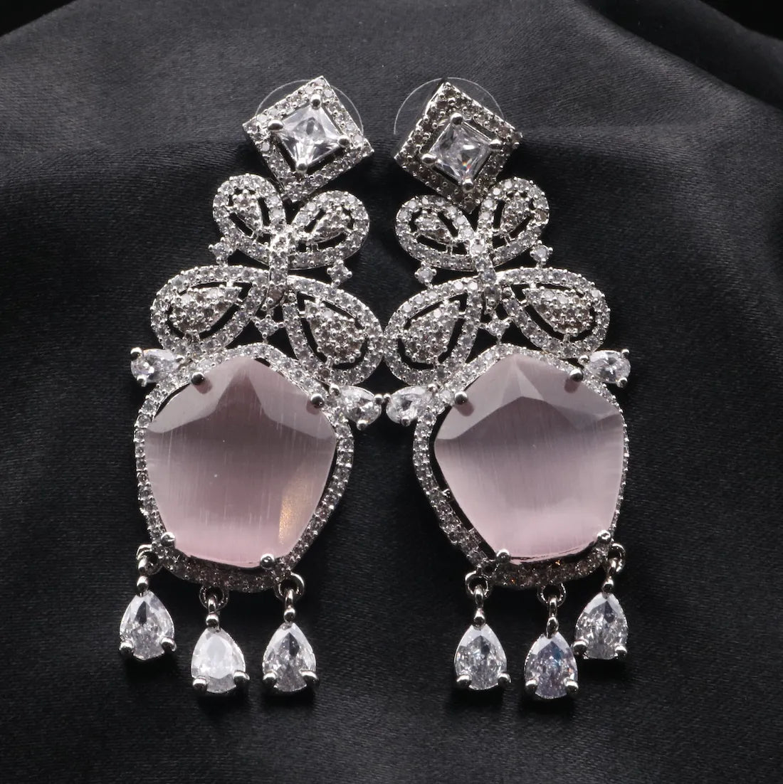 Ornate earrings with pink stones and diamond-like crystals on a dark background