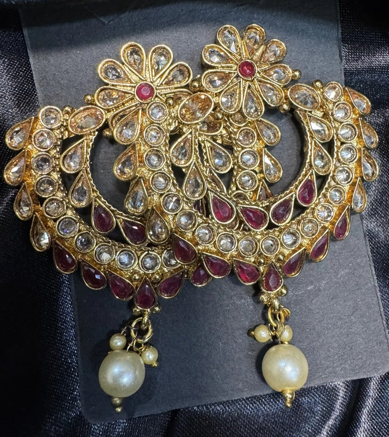 Ornate gold earrings with red stones and pearl-like beads on a dark fabric background